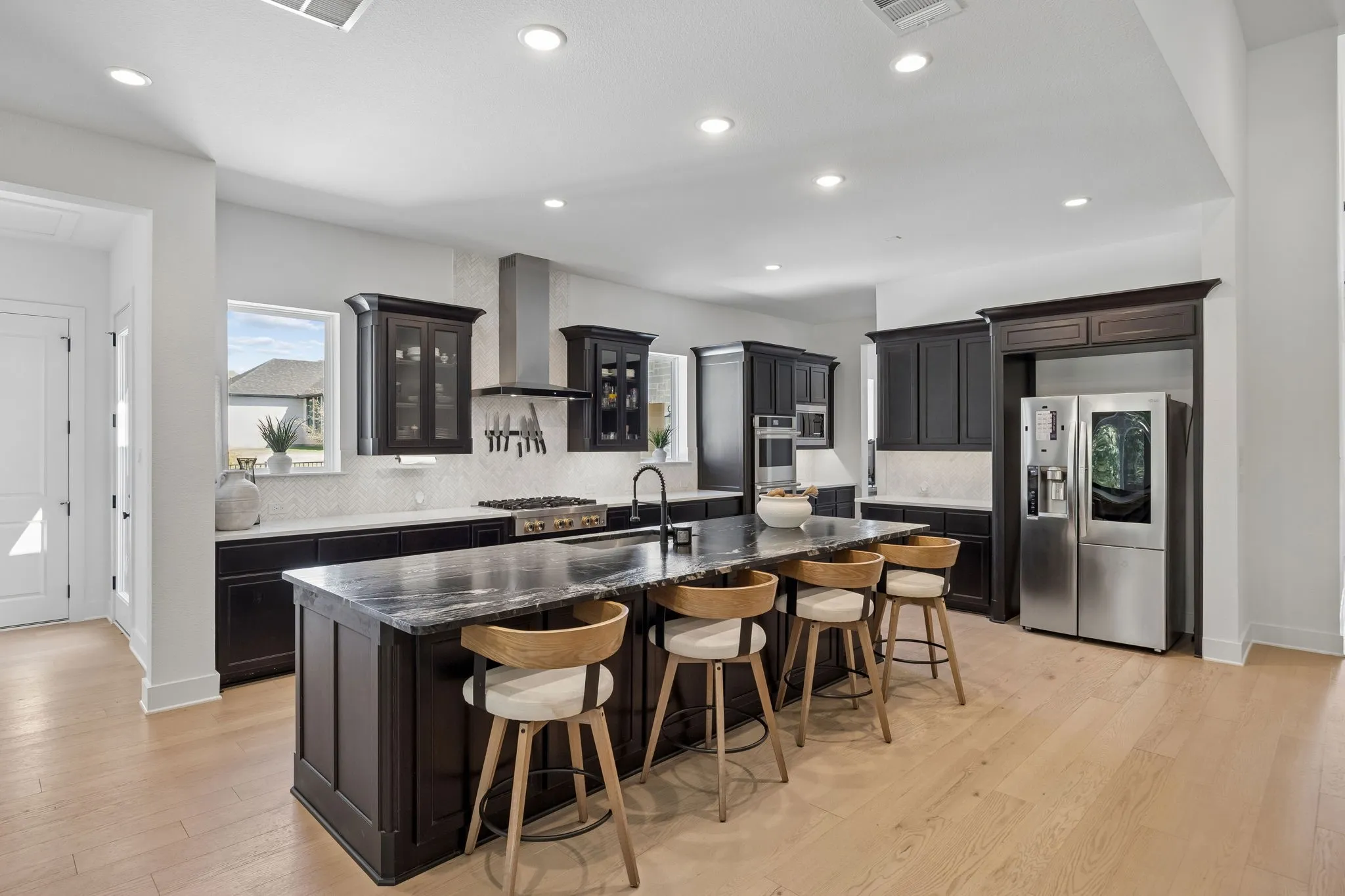 Kitchen featuring dark cabinetry, a large center island with seating, a stainless steel gas range with a hood, a stainless steel refrigerator, and light wood-finish flooring