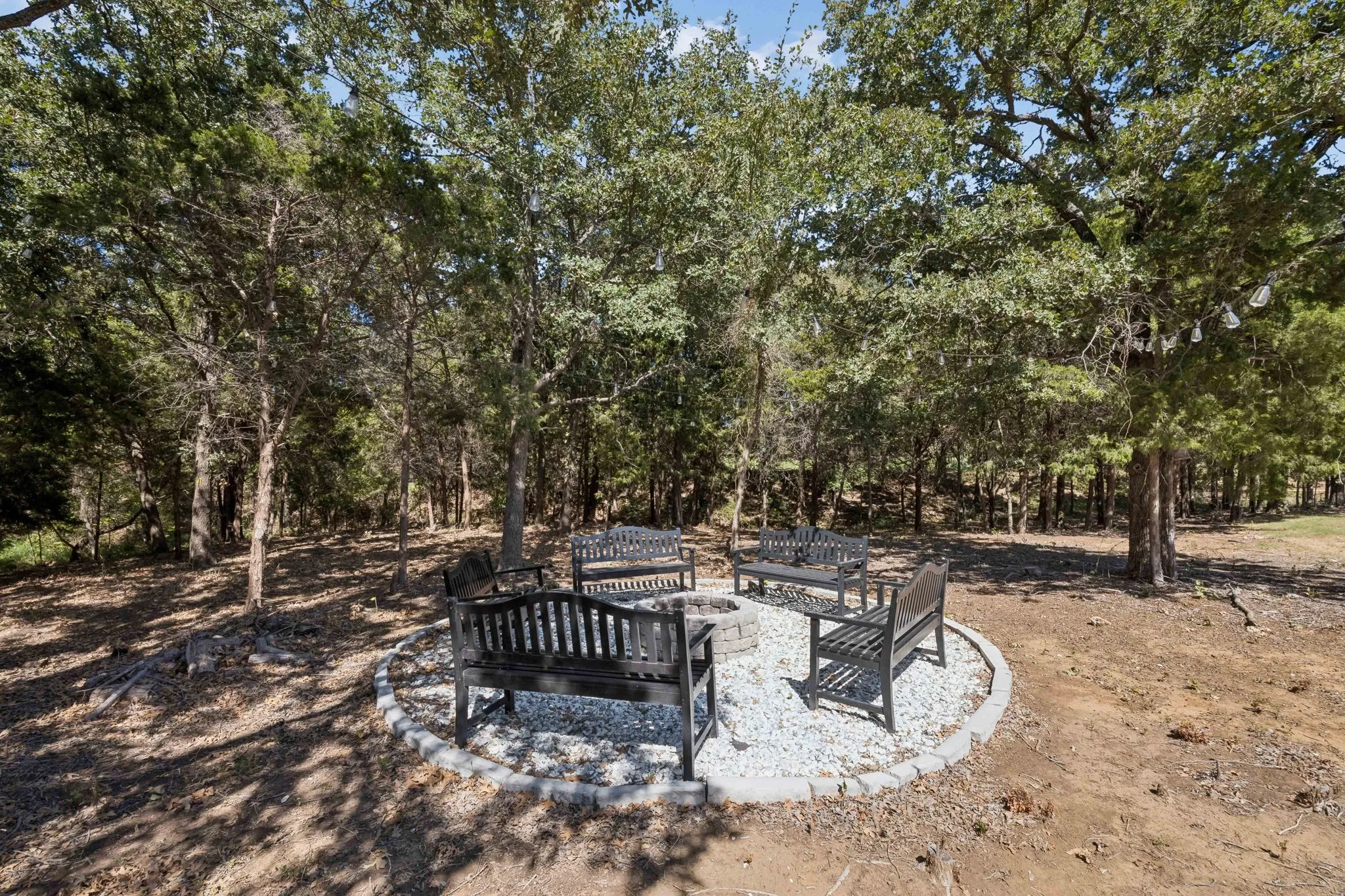 Outdoor gathering area featuring a circular fire pit with surrounding benches, bordered by stone pavers