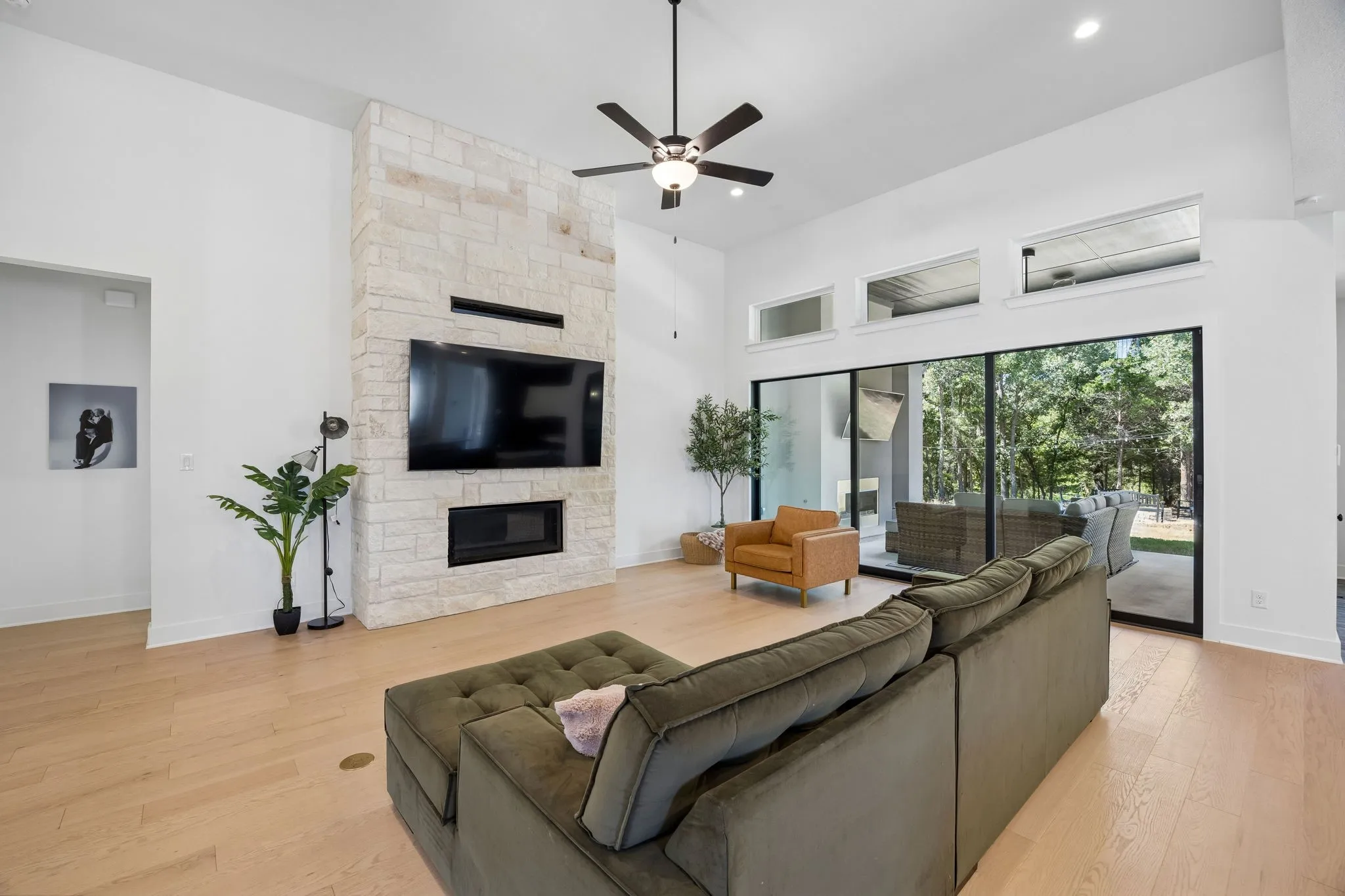 High vaulted ceiling, stone-clad fireplace, built-in fireplace, expansive sliding glass doors, upper transom windows, and light wood-finish flooring