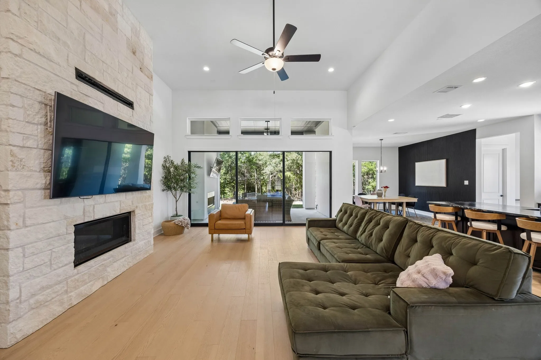 Stone-clad fireplace with an integrated linear firebox, high ceilings with recessed lighting, wood-finish flooring, and large sliding glass doors