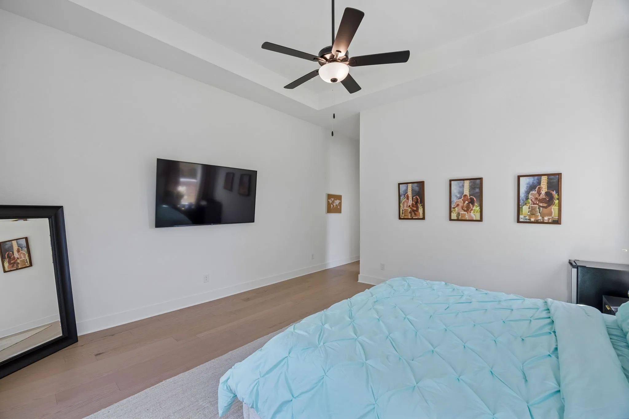 Tray ceiling with a ceiling fan, light wood-finish flooring, and white walls