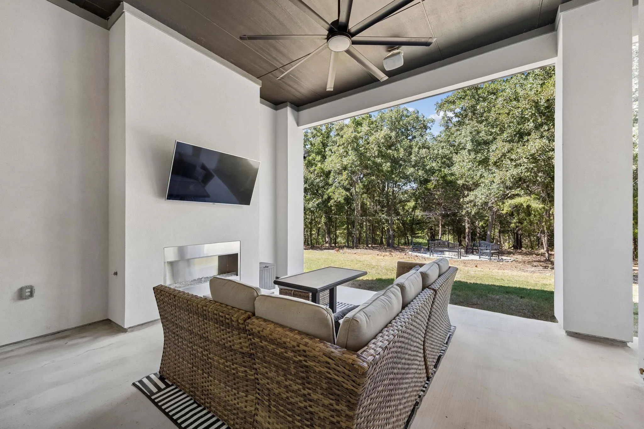 Expansive covered patio featuring a mounted television, linear fireplace, ceiling fan, and concrete flooring