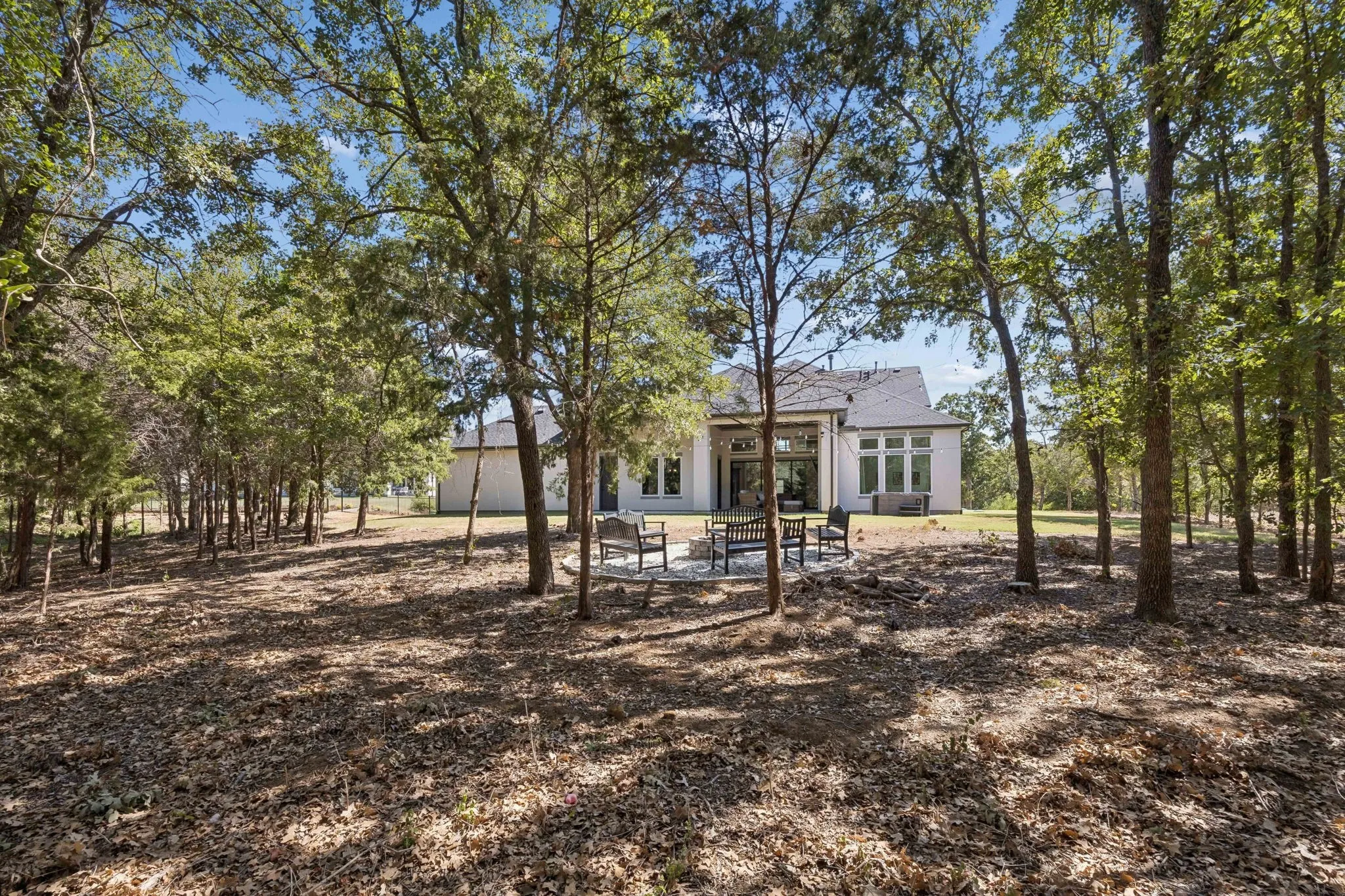 Wooded grounds with a stone patio and exterior lighting, featuring a white painted brick facade and a dark shingle roof