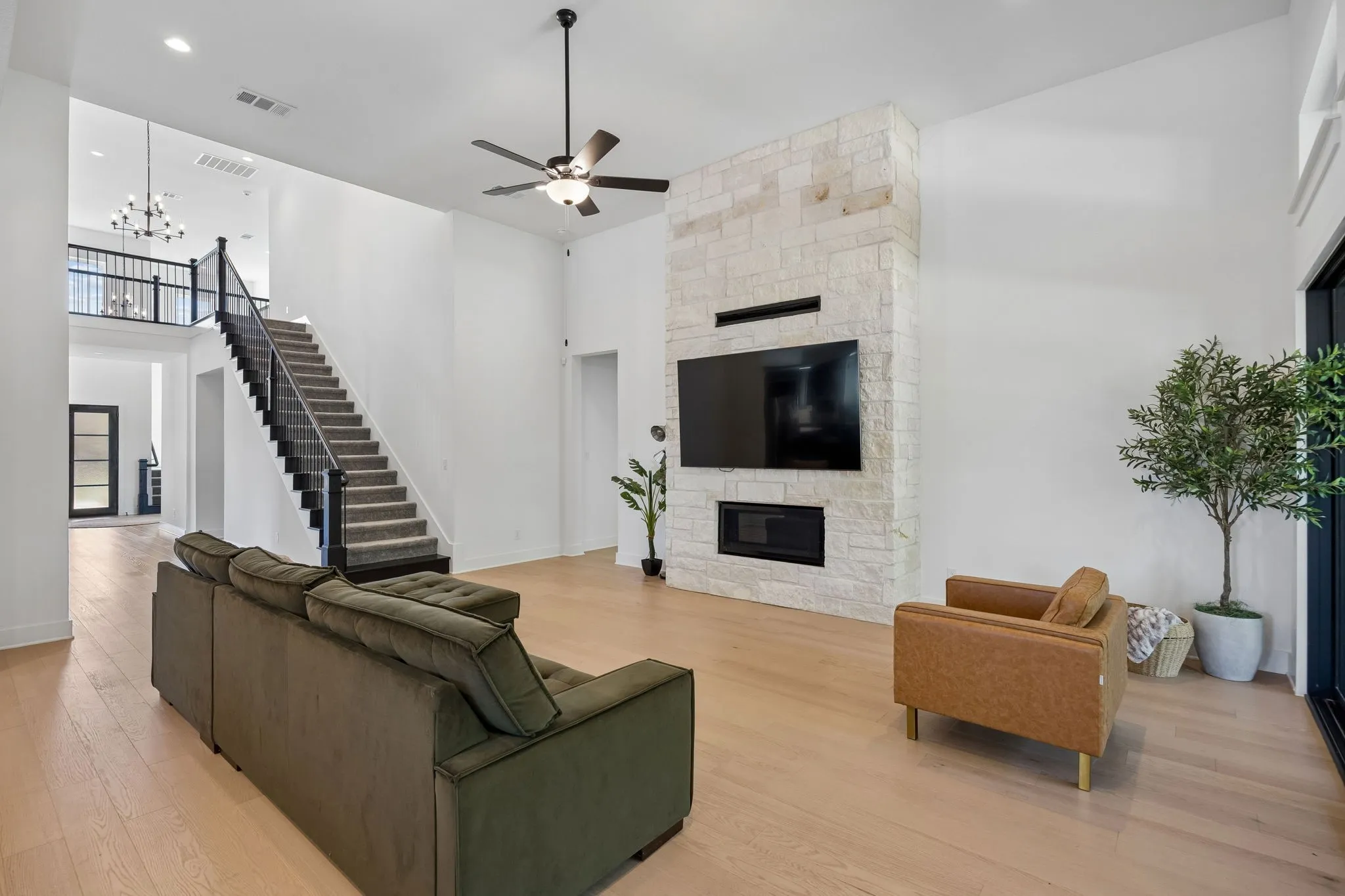 Spacious living area featuring light wood-finish flooring, a stone-clad fireplace with a built-in media niche, and a ceiling fan