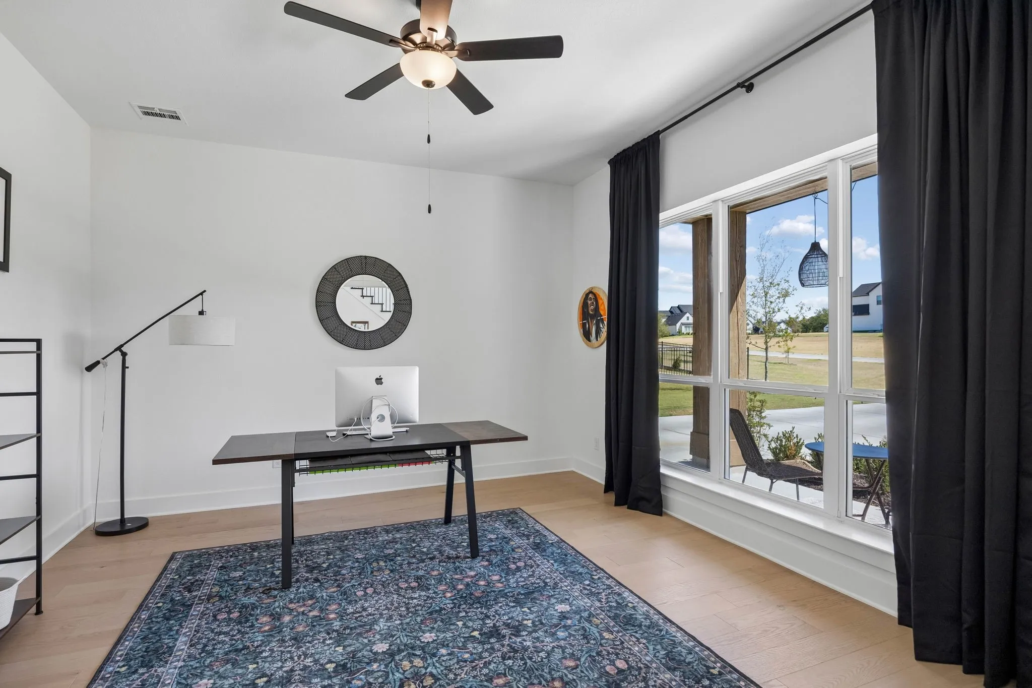 Light wood-finish flooring, a ceiling fan with integrated lighting, and a large multi-pane window with dark drapery
