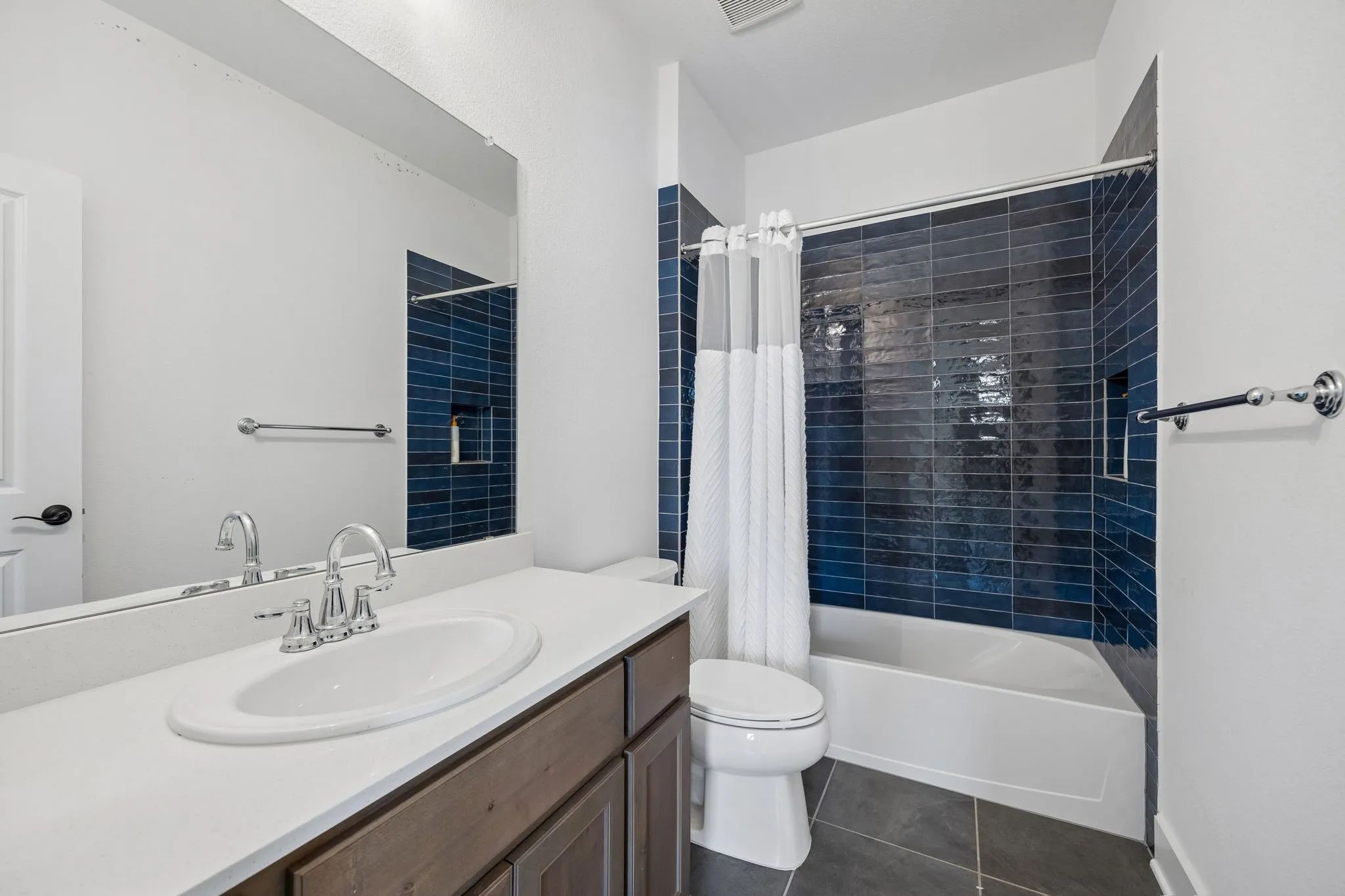Bathroom featuring a wood-finish vanity with an integrated sink, polished chrome faucet, large vanity mirror, and a tub with blue subway tile surround