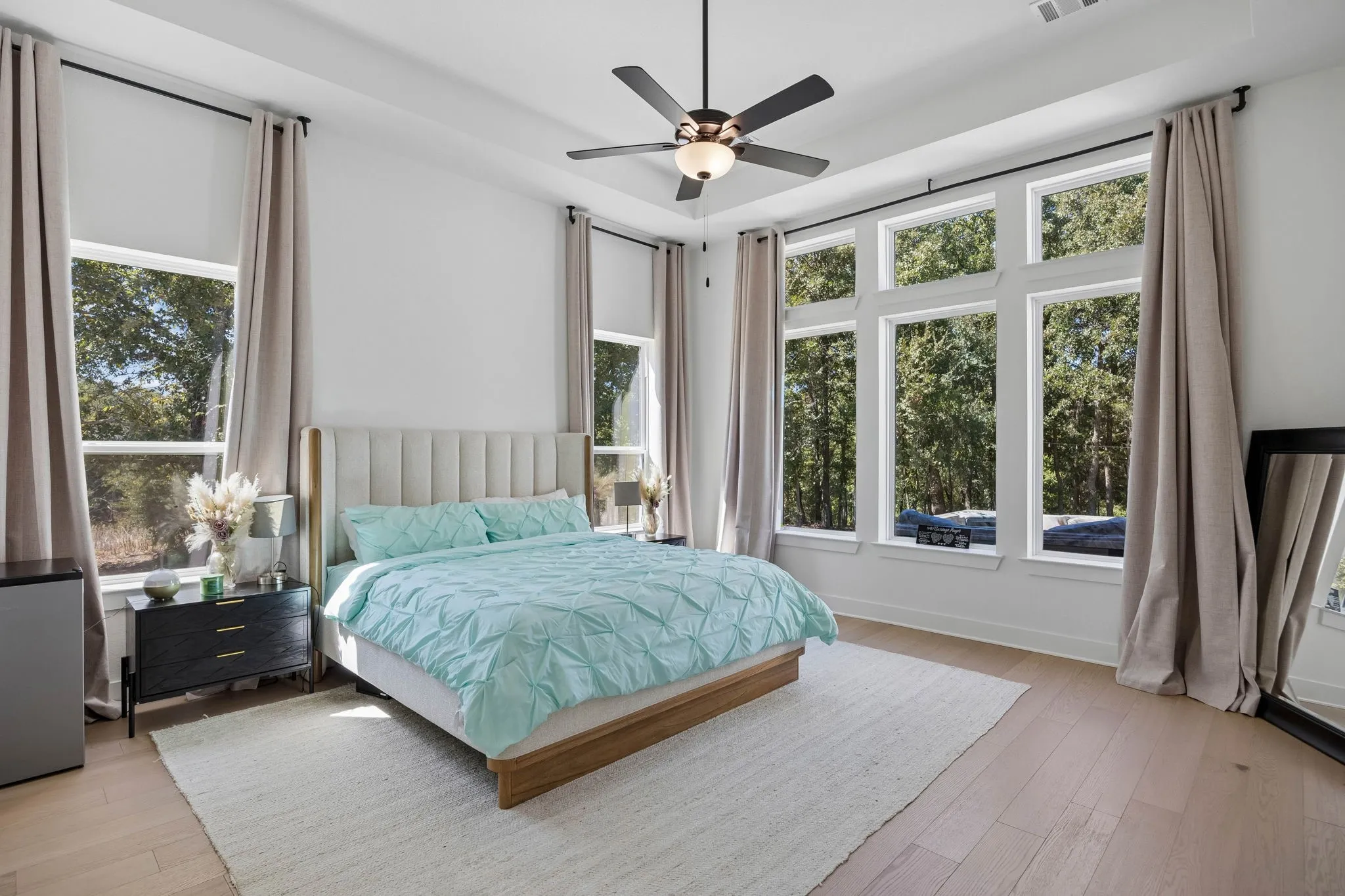 Recessed ceiling with a central fan light fixture, wood-finish flooring, and multiple large windows with roller shades
