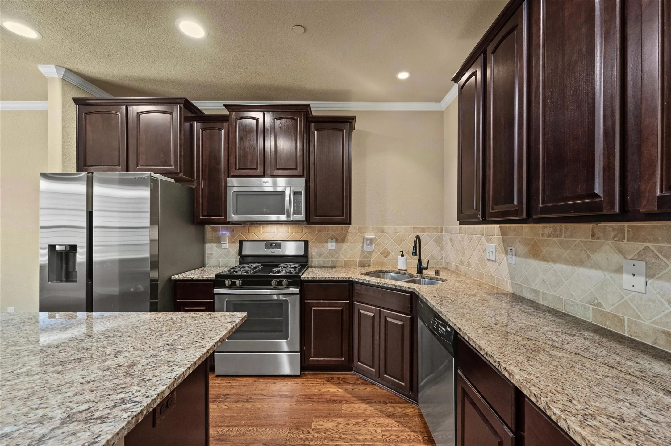 Kitchen featuring rich wood cabinetry, granite countertops, stainless steel appliances, a tile backsplash, and wood-finish flooring