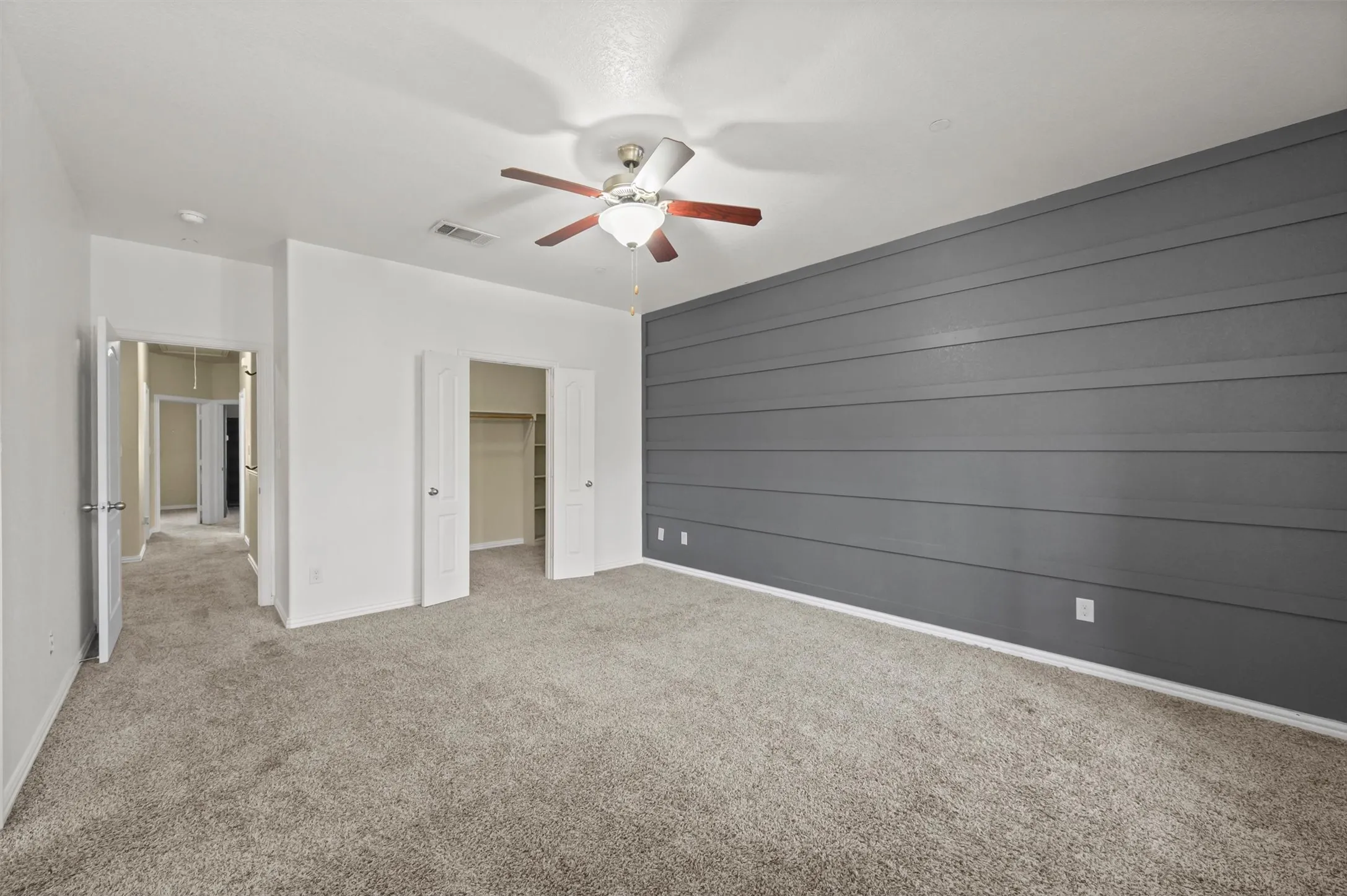 Spacious room featuring a horizontal shiplap accent wall, plush carpet, and a ceiling fan with integrated lighting