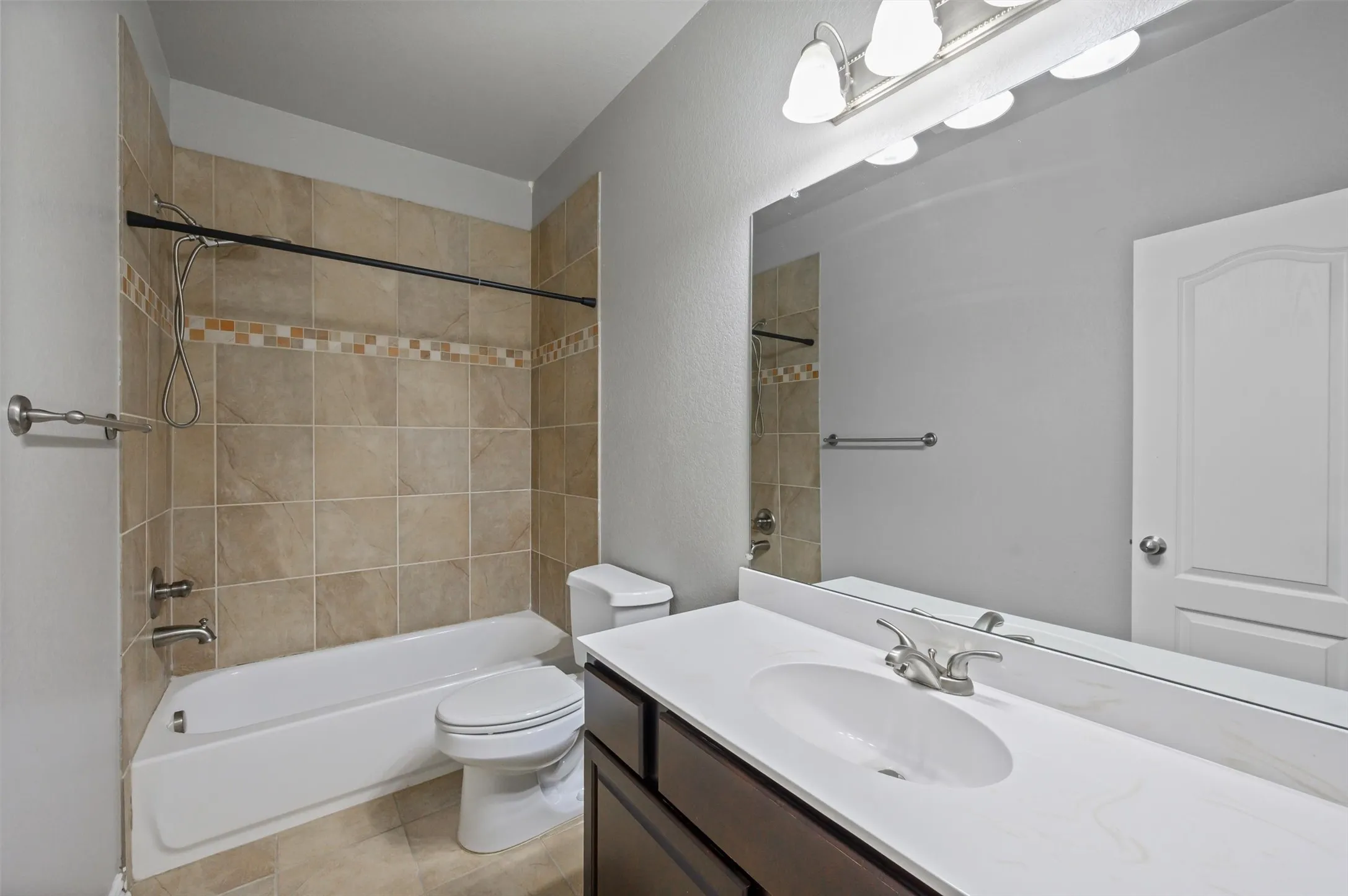 Bathroom featuring a built-in tub with tile surround, tile flooring, a single vanity with an integrated sink, and an arched panel door