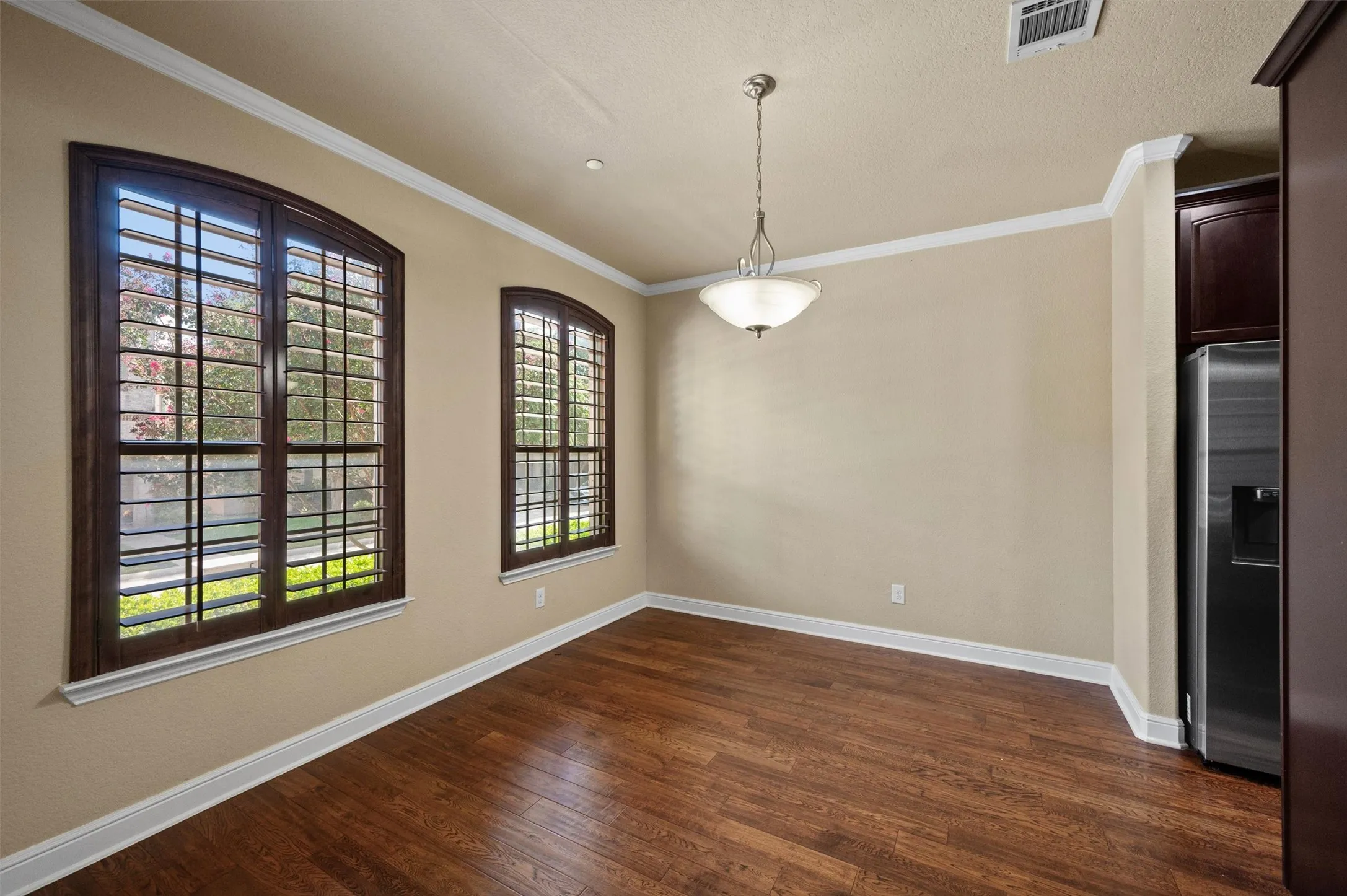 Hardwood-style flooring, crown molding, two arched windows with plantation shutters, ceiling-mounted light fixture, and recessed lighting
