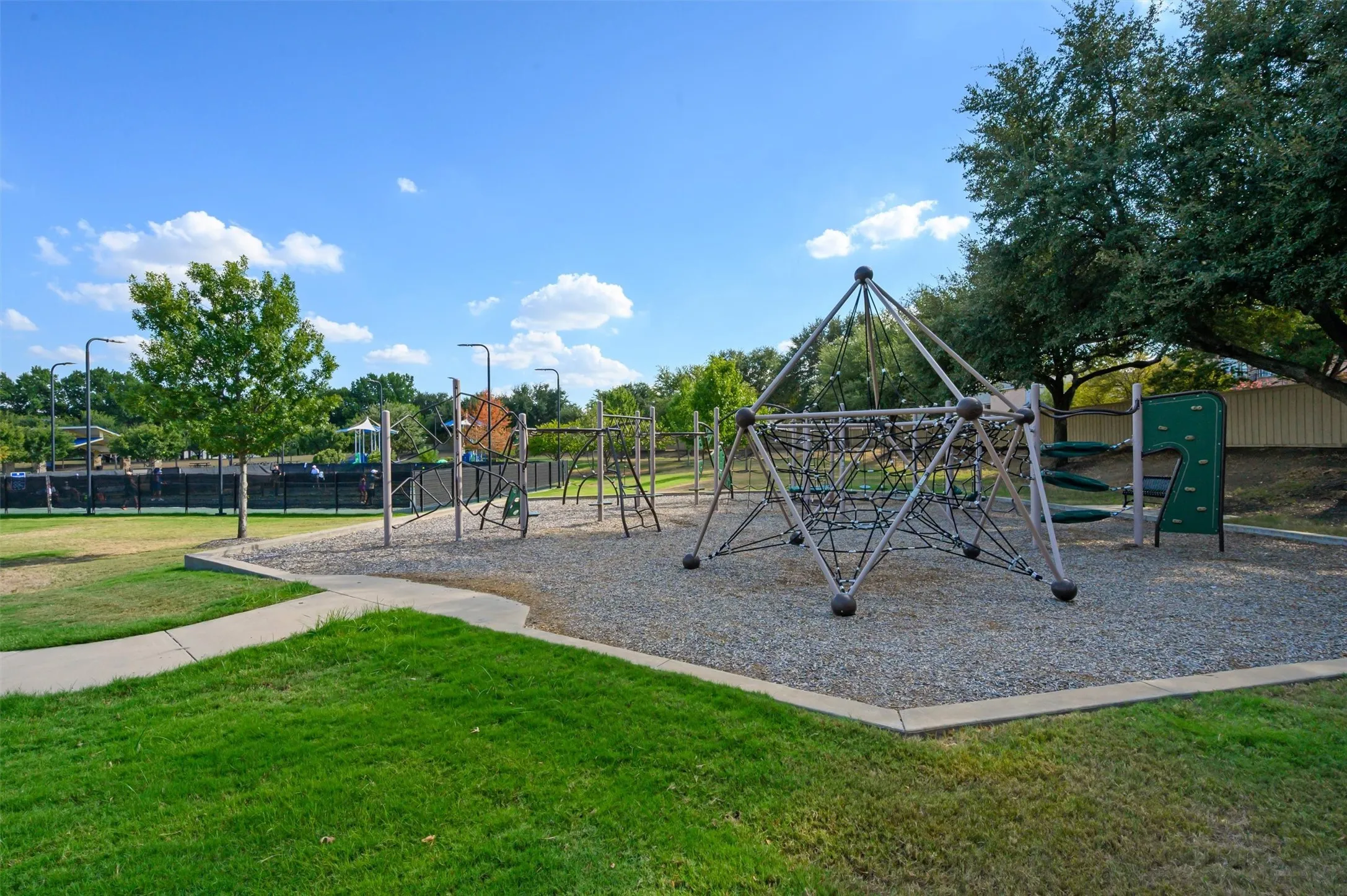 Community playground featuring a climbing structure, swings, and a recreational court in the background