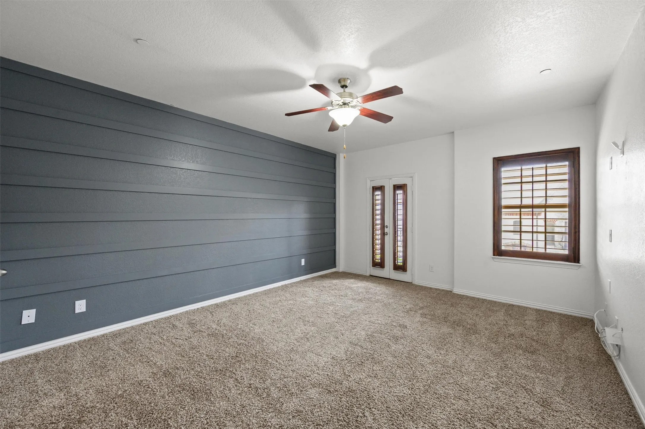 Textured accent wall, ceiling fan, carpet flooring, dual-pane window, exterior door with glass inserts