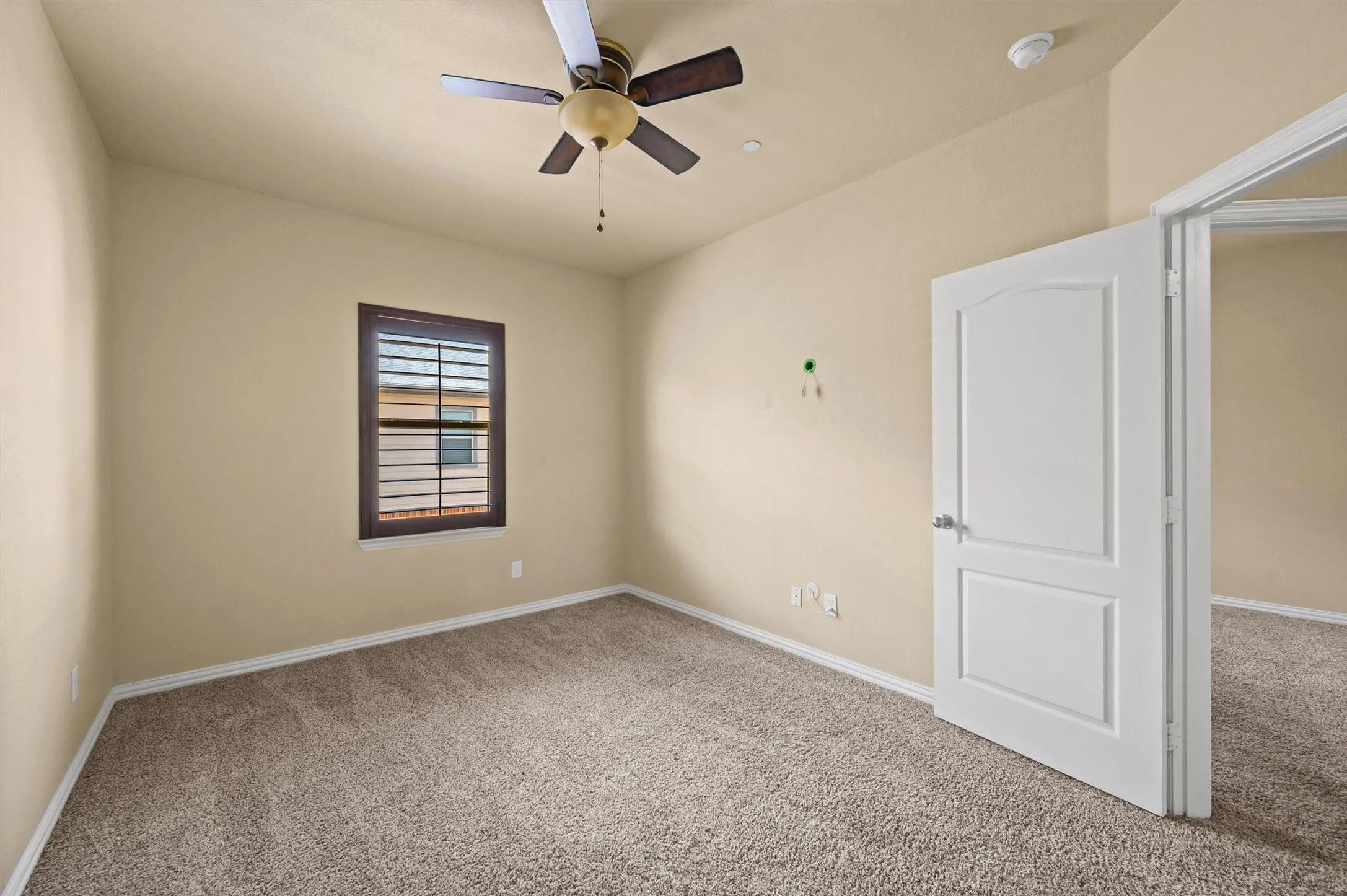 Carpeted flooring, neutral wall tones, window with horizontal blinds, ceiling fan, and a paneled door with brushed nickel hardware