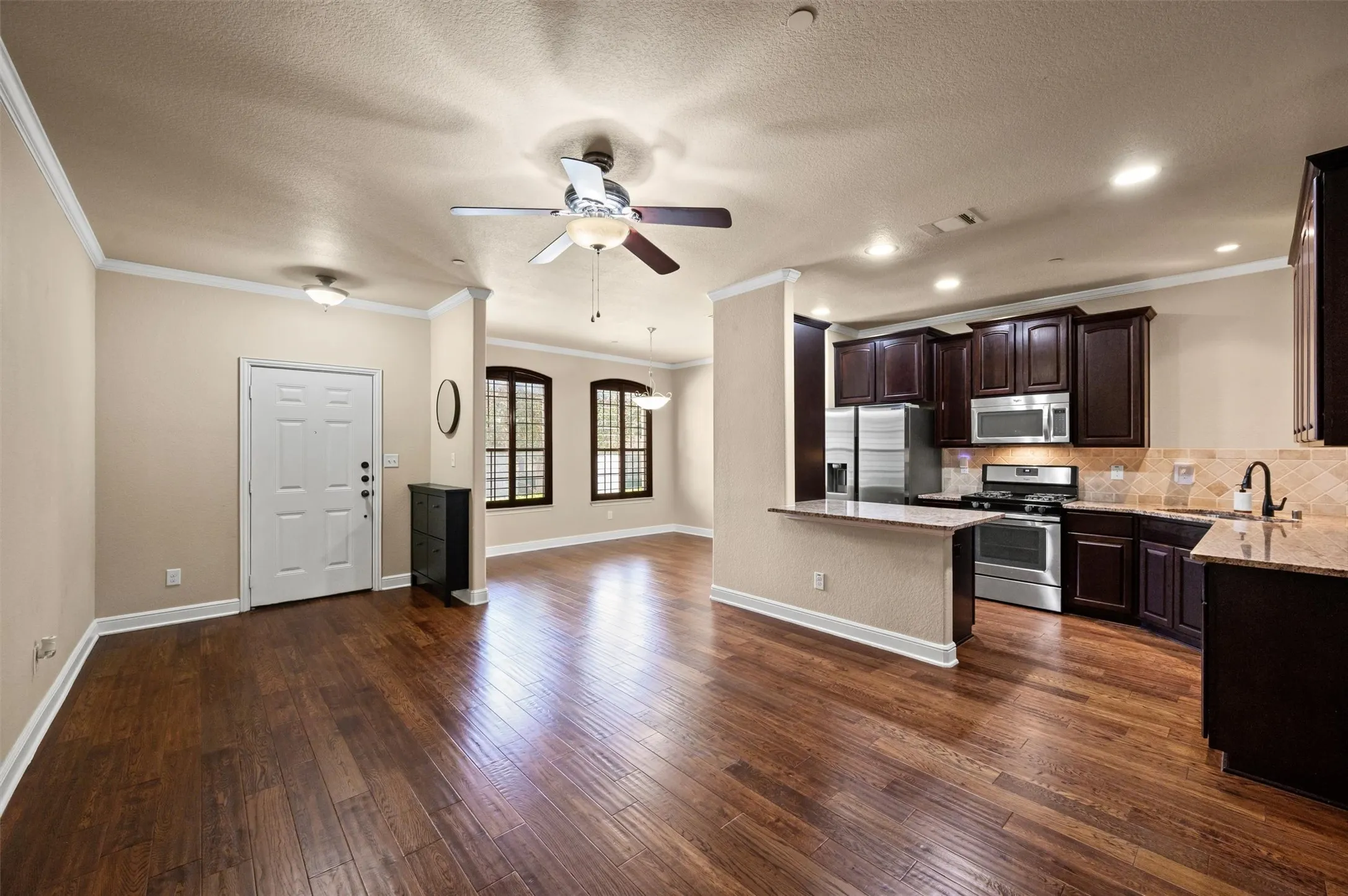 Wood-finish flooring throughout, kitchen with dark wood cabinetry, stainless steel appliances, and a breakfast bar