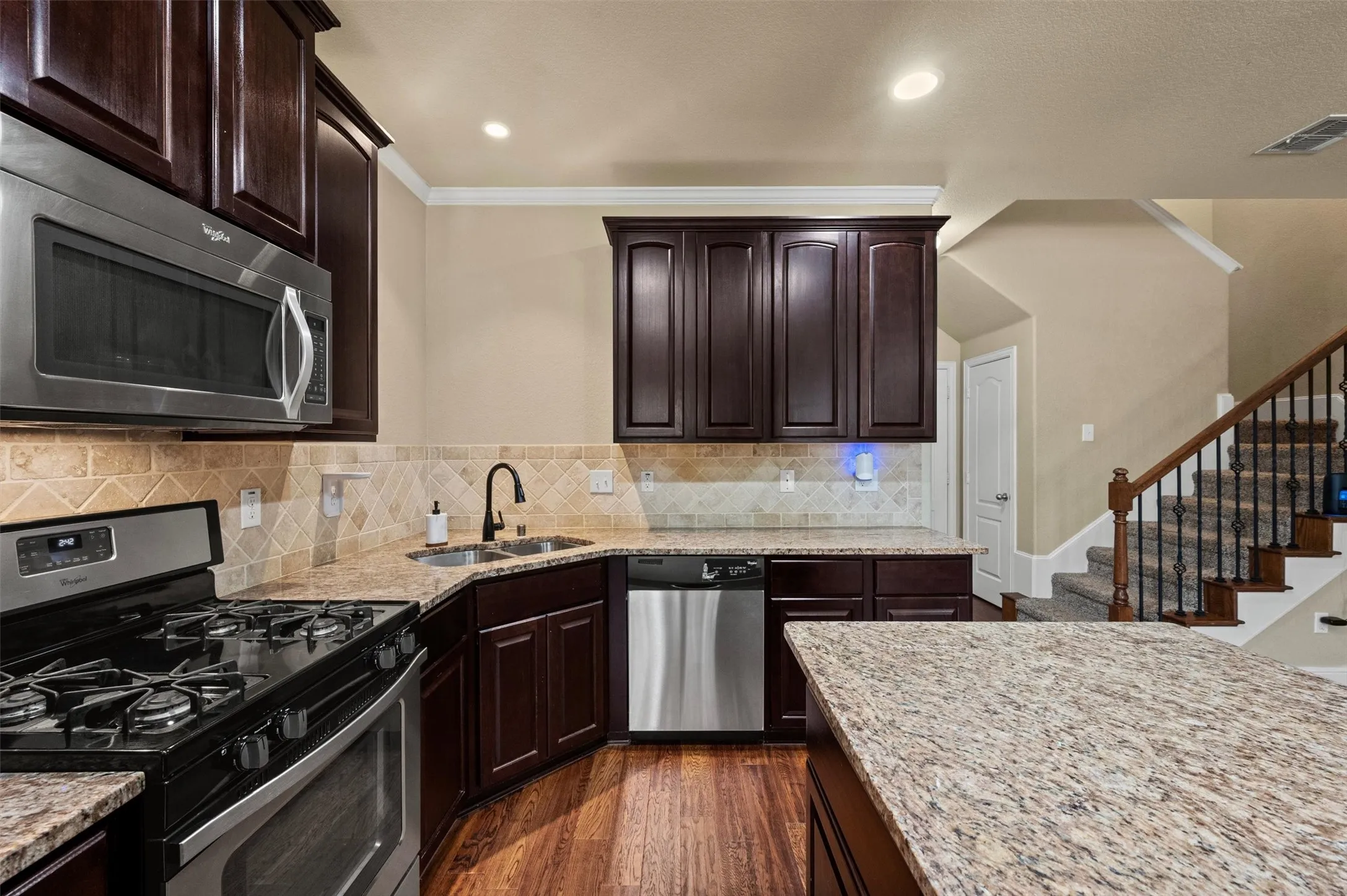 Dark wood-finish cabinetry, stainless steel appliances, granite countertops, tile backsplash, and wood-finish flooring