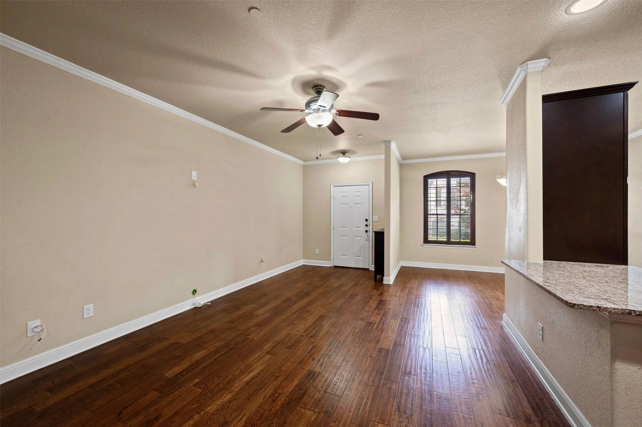 Wood-finish flooring, crown molding, built-in ceiling fans, arched window with grilles, and a stone-finish countertop