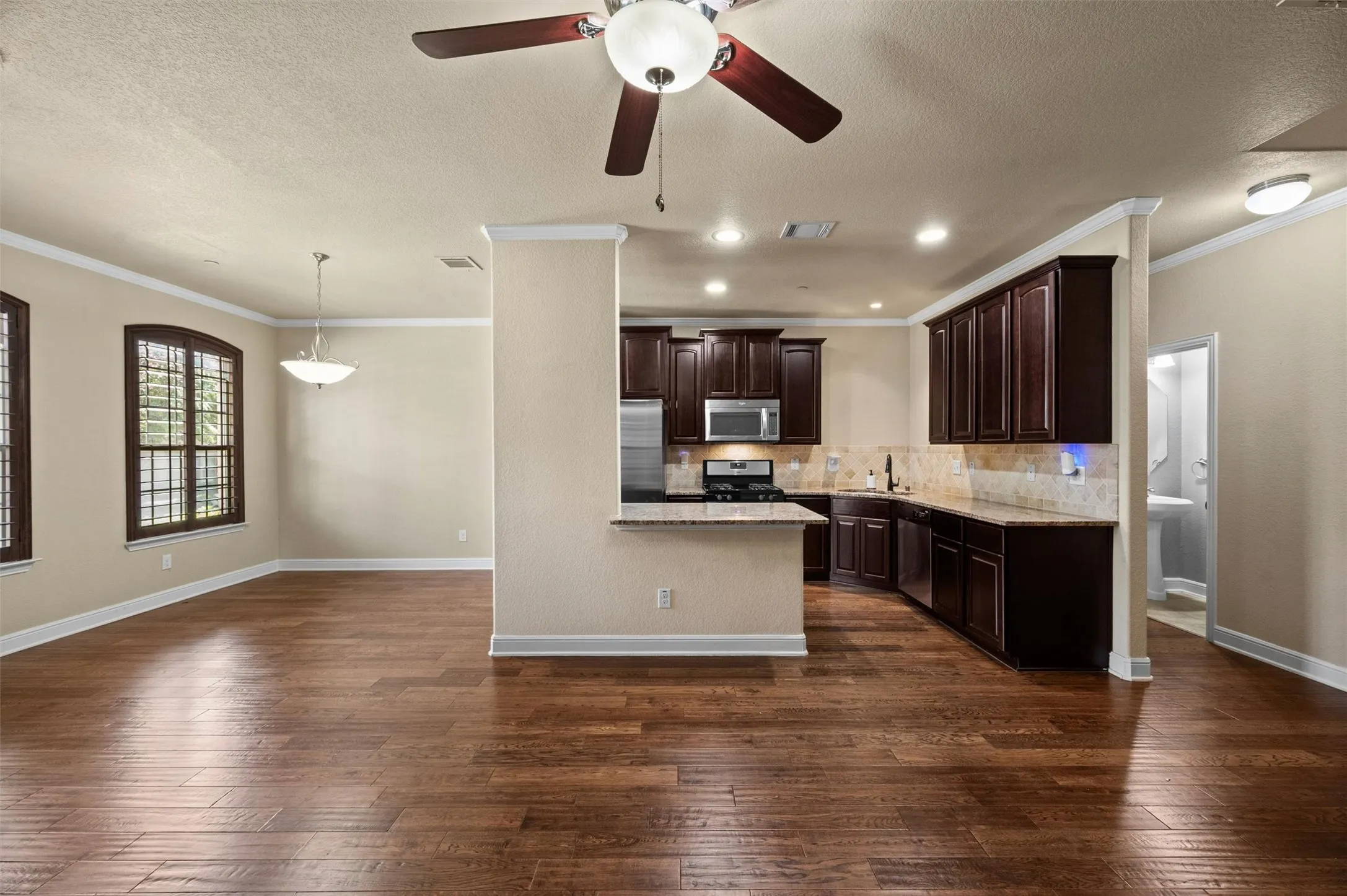 Wood-finish flooring throughout, dark wood cabinetry, stainless steel appliances, breakfast bar, and recessed lighting
