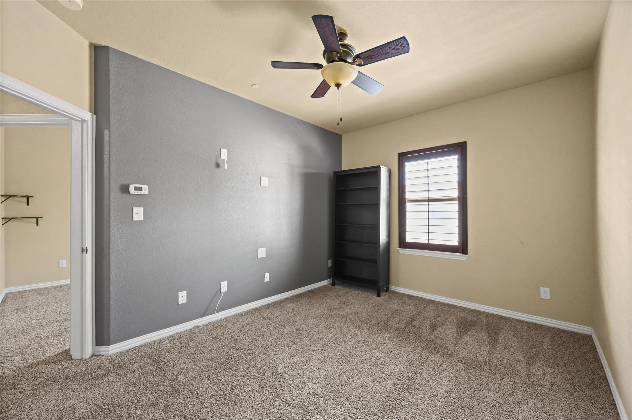 Carpeted flooring, ceiling fan, window with shutters, and a neutral wall color