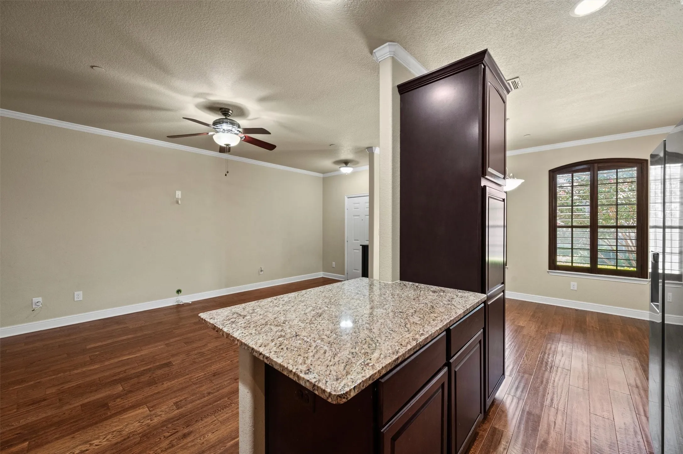Kitchen island with granite countertop, dark wood-finish cabinetry, and wood-finish flooring