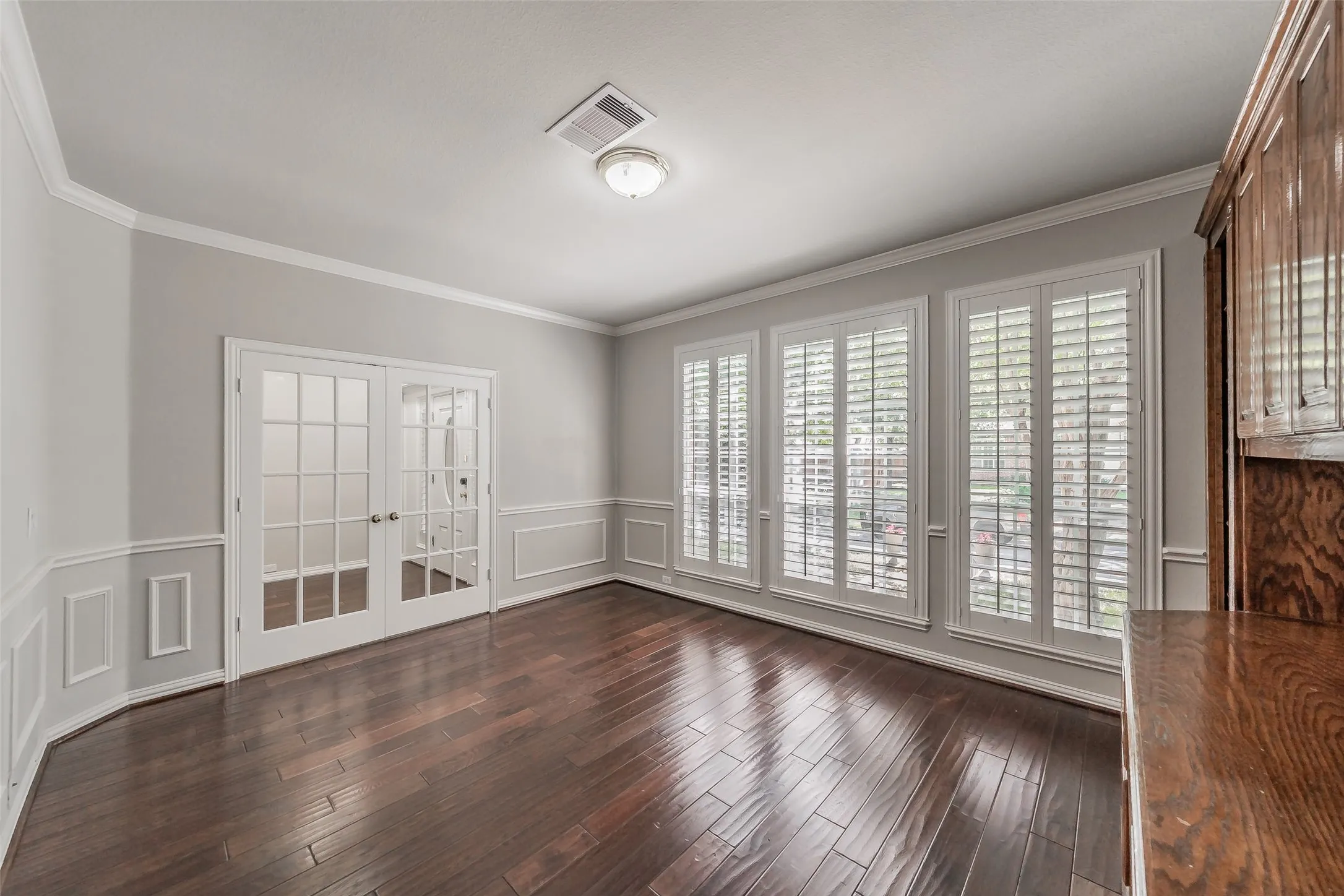 Hardwood-finish flooring, white wall paneling, crown molding, French doors with glass panes, and multiple windows with plantation shutters