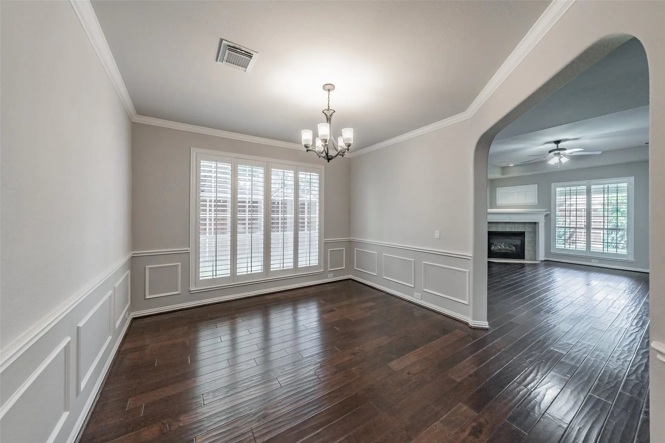 Wood-finish flooring, wainscoting, crown molding, plantation shutters, and a chandelier