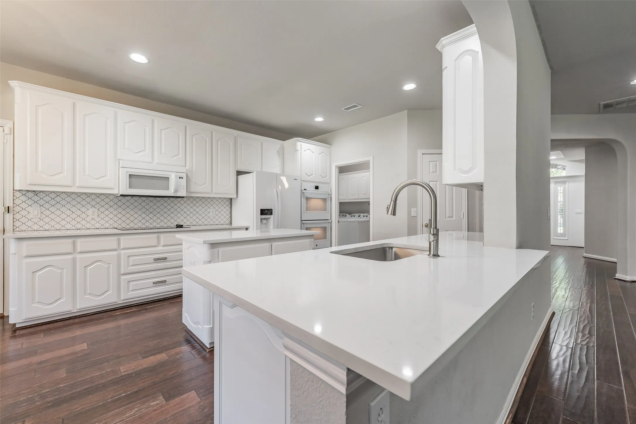Kitchen featuring two islands with solid surface countertops, extensive white cabinetry, a tile backsplash, and wood-finish flooring