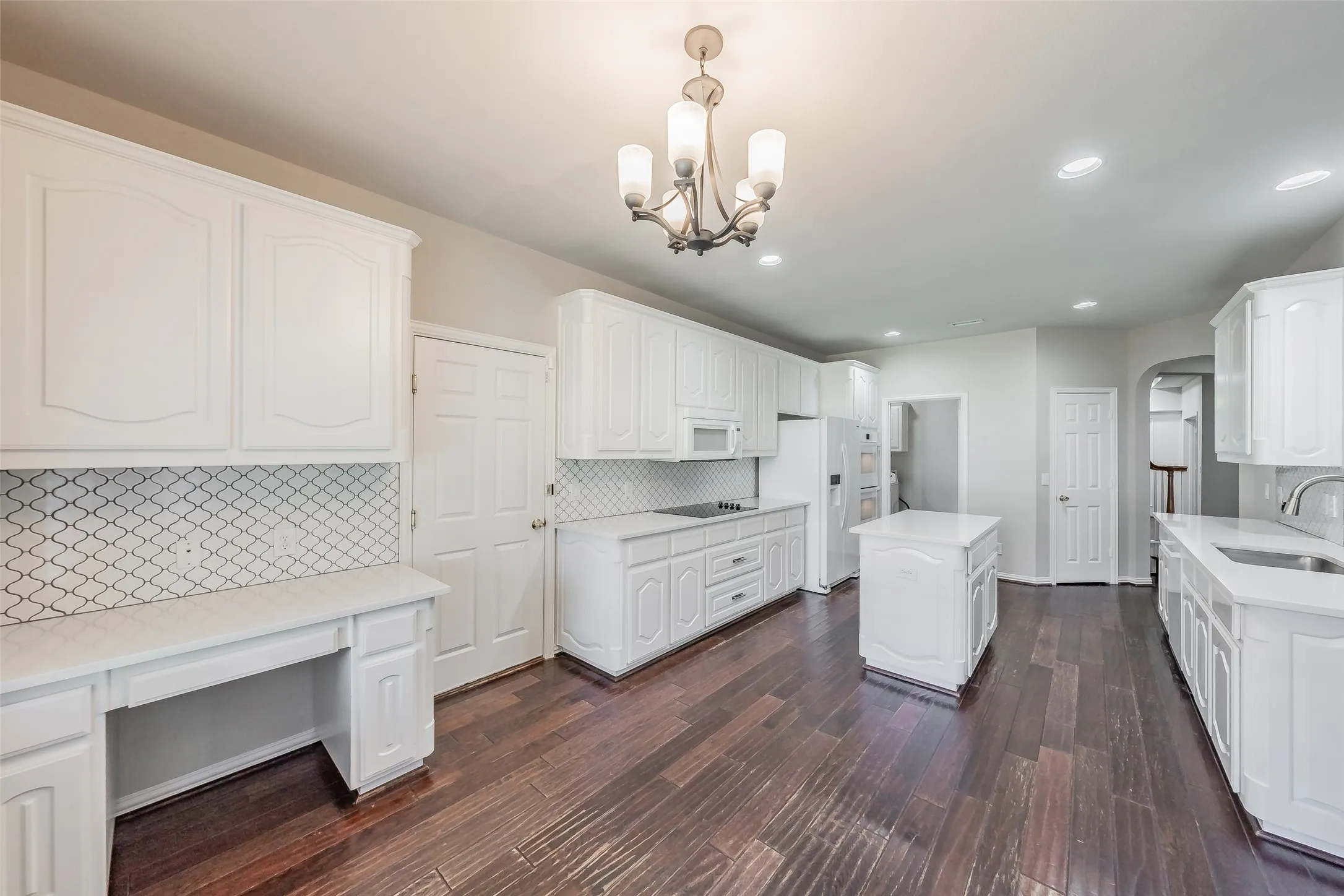 Spacious kitchen featuring extensive white cabinetry, a center island, dark wood-finish flooring, and a decorative tile backsplash