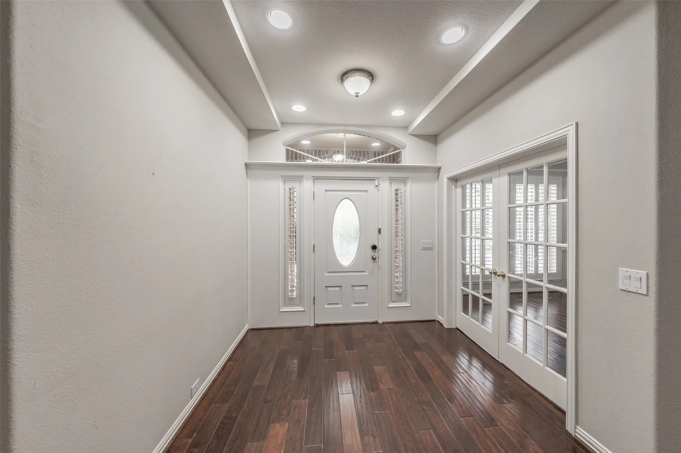 Entryway featuring wood-finish flooring, recessed lighting, white French doors, and a decorative transom window