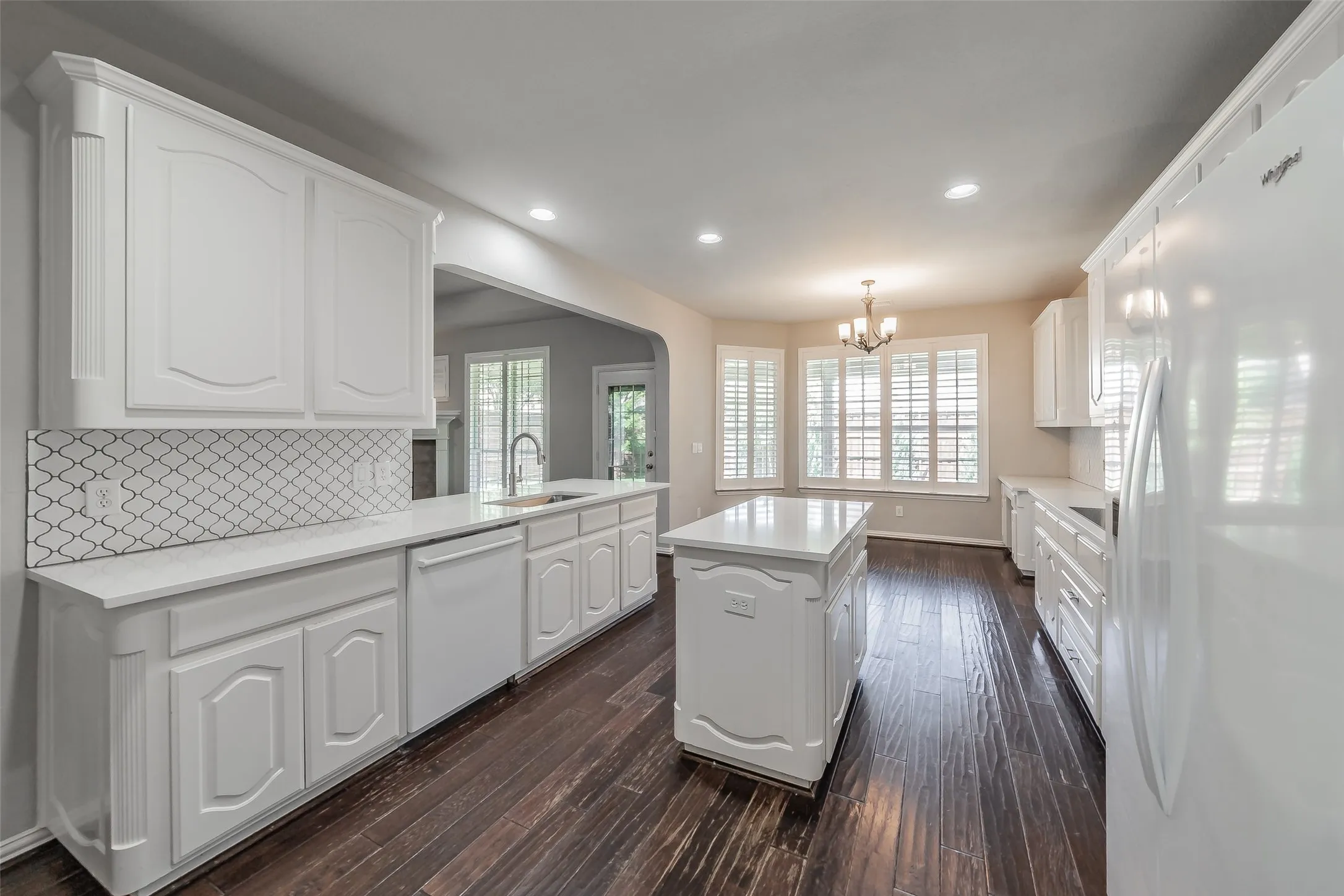 Kitchen featuring white cabinetry, light countertops, arabesque tile backsplash, a central island, and wood-finish flooring