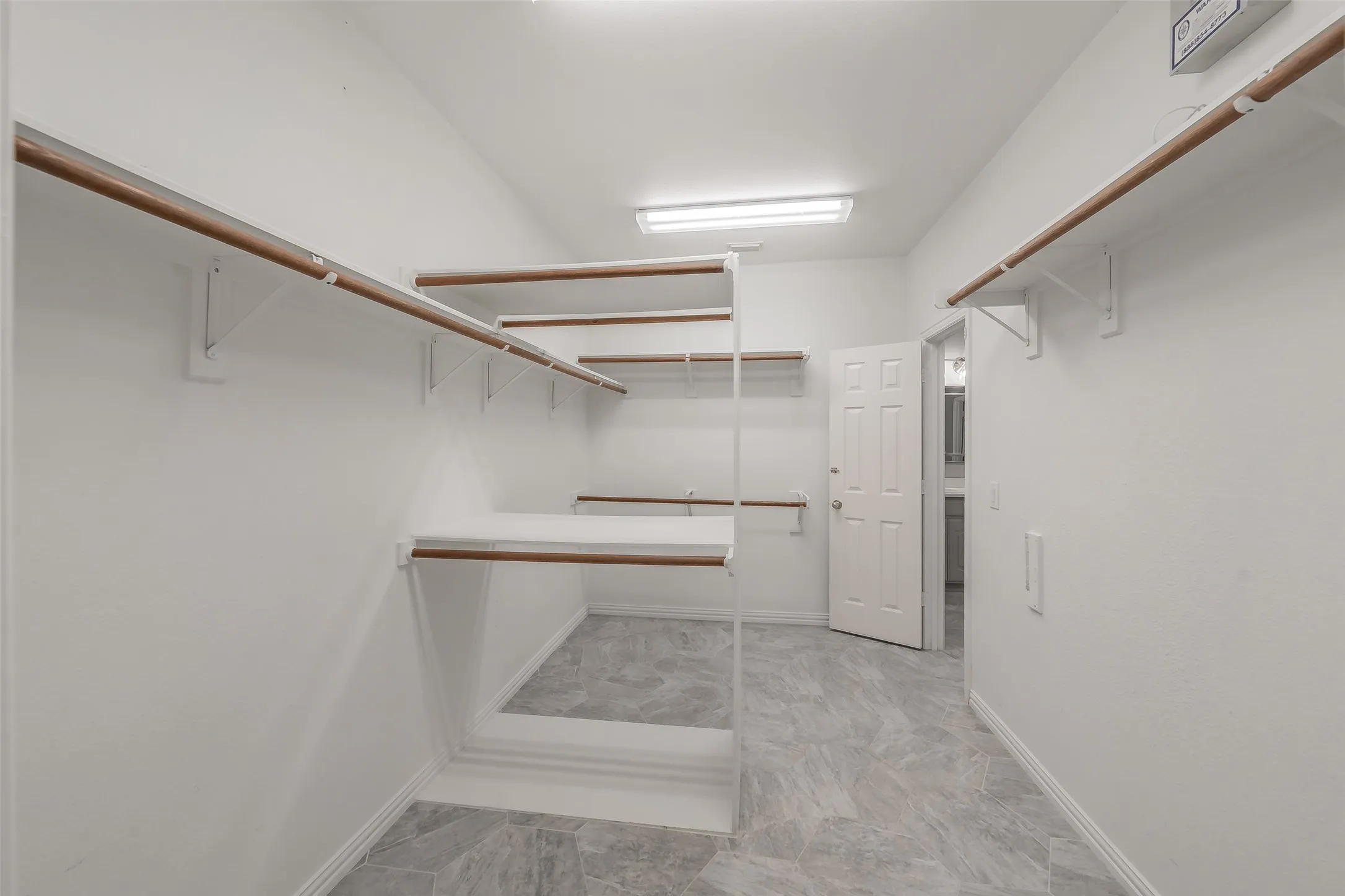 Spacious walk-in closet with multiple hanging rods and shelves, illuminated by overhead fluorescent lighting