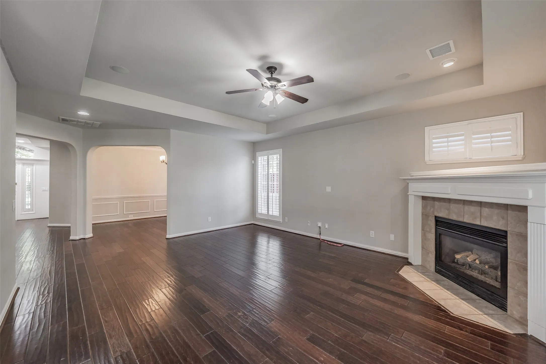 Spacious room featuring wood-finish flooring, a tray ceiling with a ceiling fan, and recessed lighting