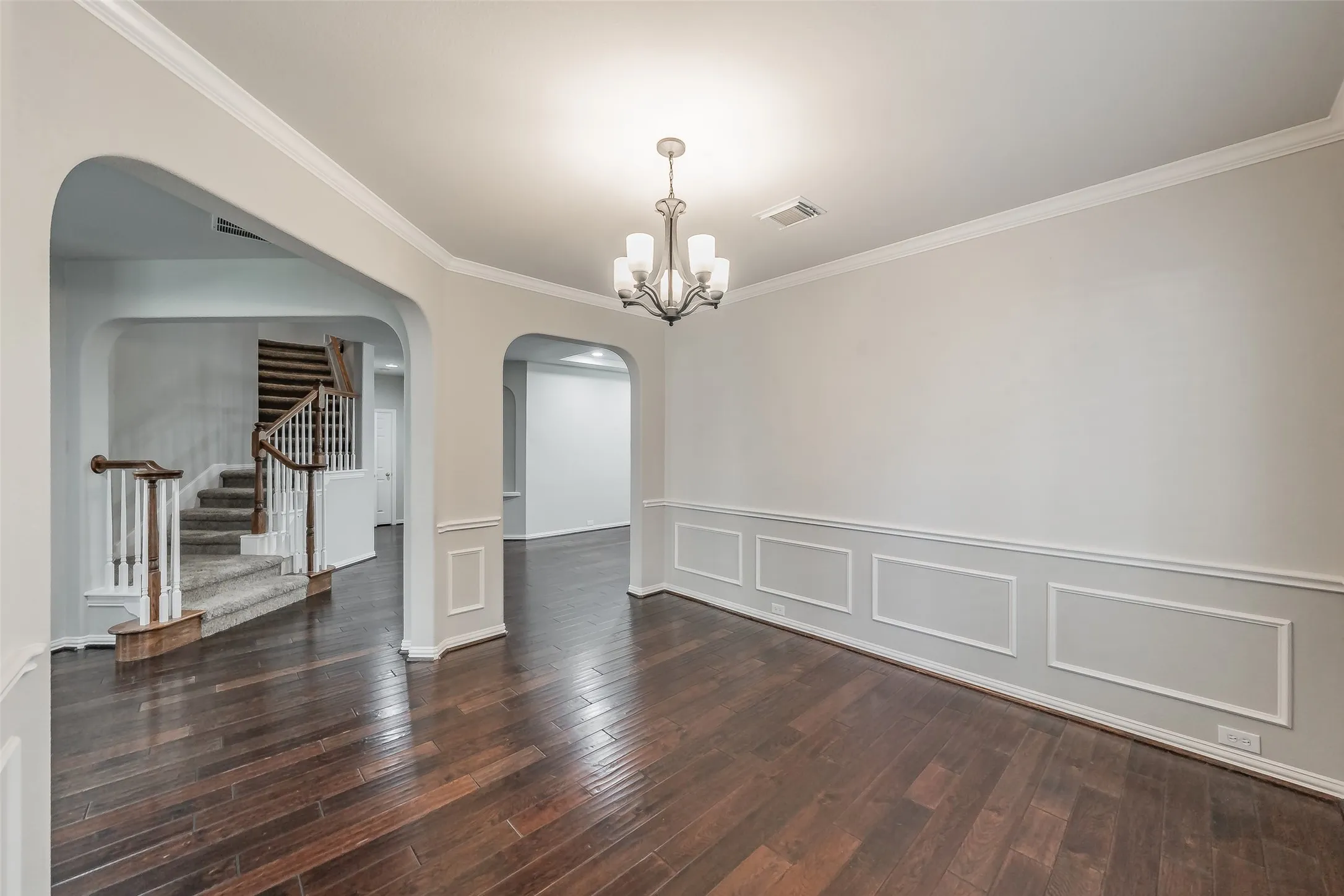 Hardwood flooring, decorative wainscoting, crown molding, arched entryways, and a chandelier