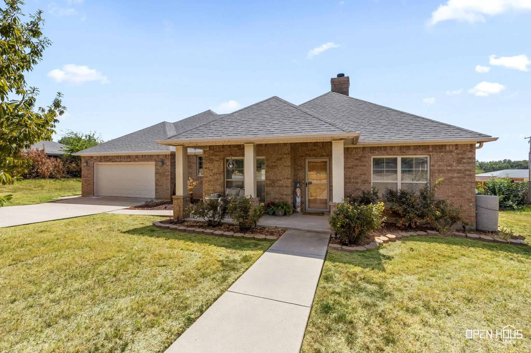 Brick facade, asphalt shingle roof, attached garage, covered front porch, and concrete walkway