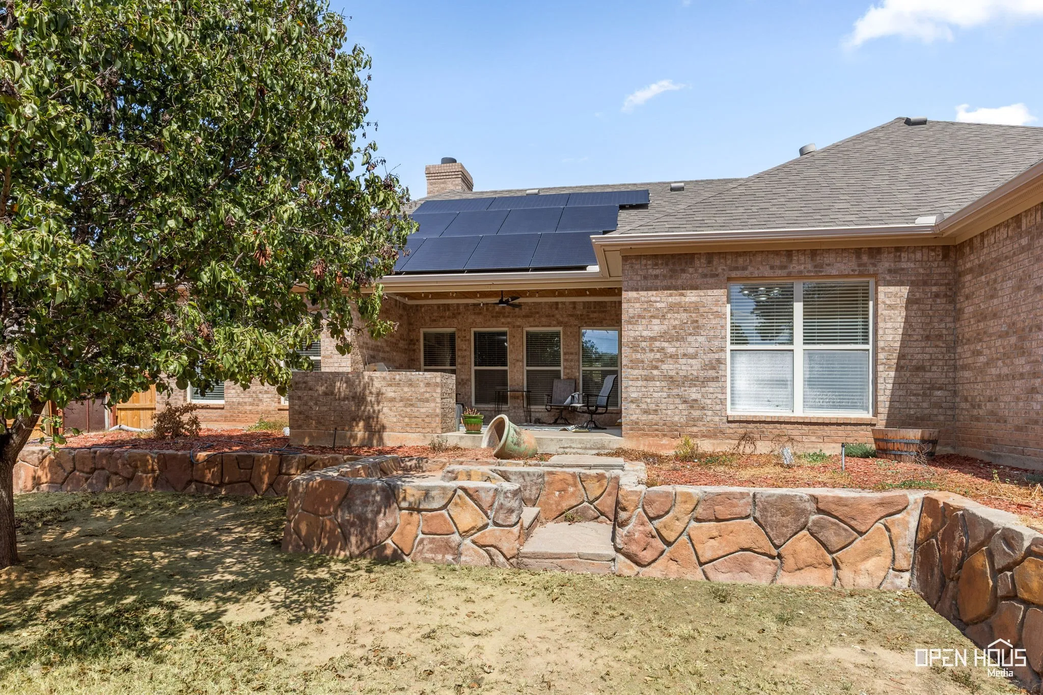 Brick exterior with a covered patio, integrated solar panels, and tiered stone retaining walls