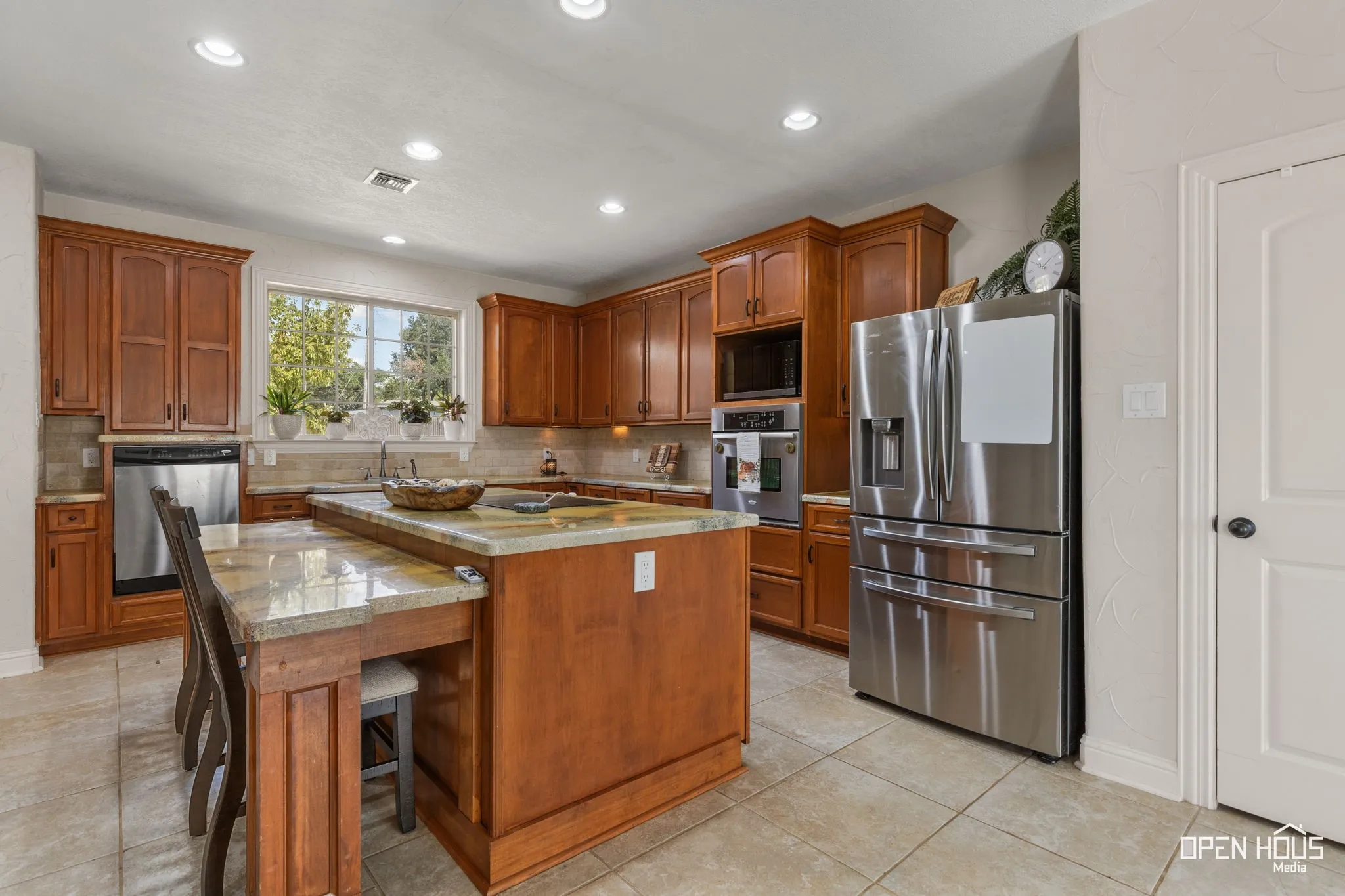 Central kitchen island with granite countertop, recessed lighting, wood cabinetry, stainless steel appliances, and tile flooring
