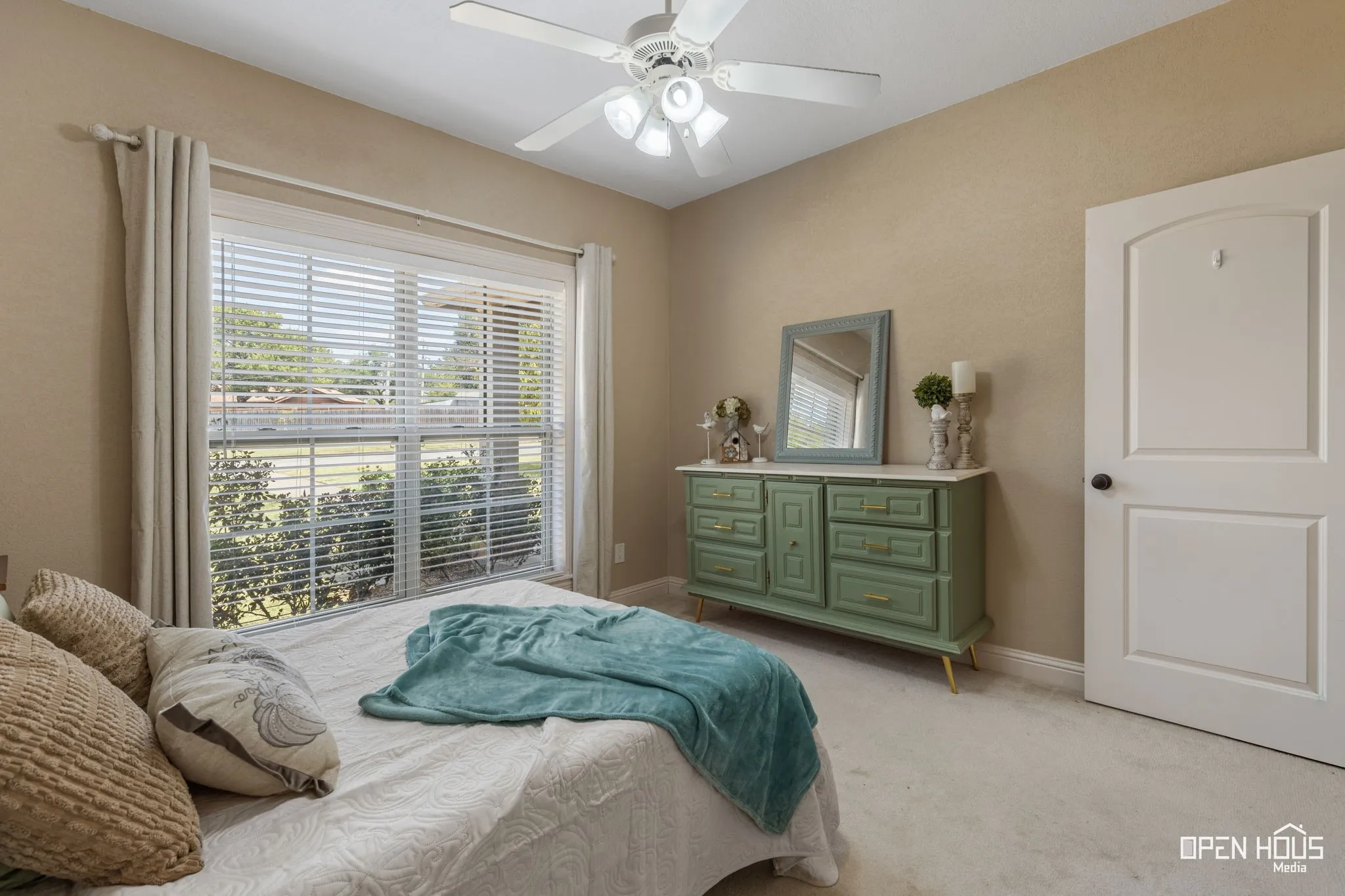 Wall-to-wall carpeting, window with blinds and curtains, ceiling fan with integrated lighting, and an arched panel door