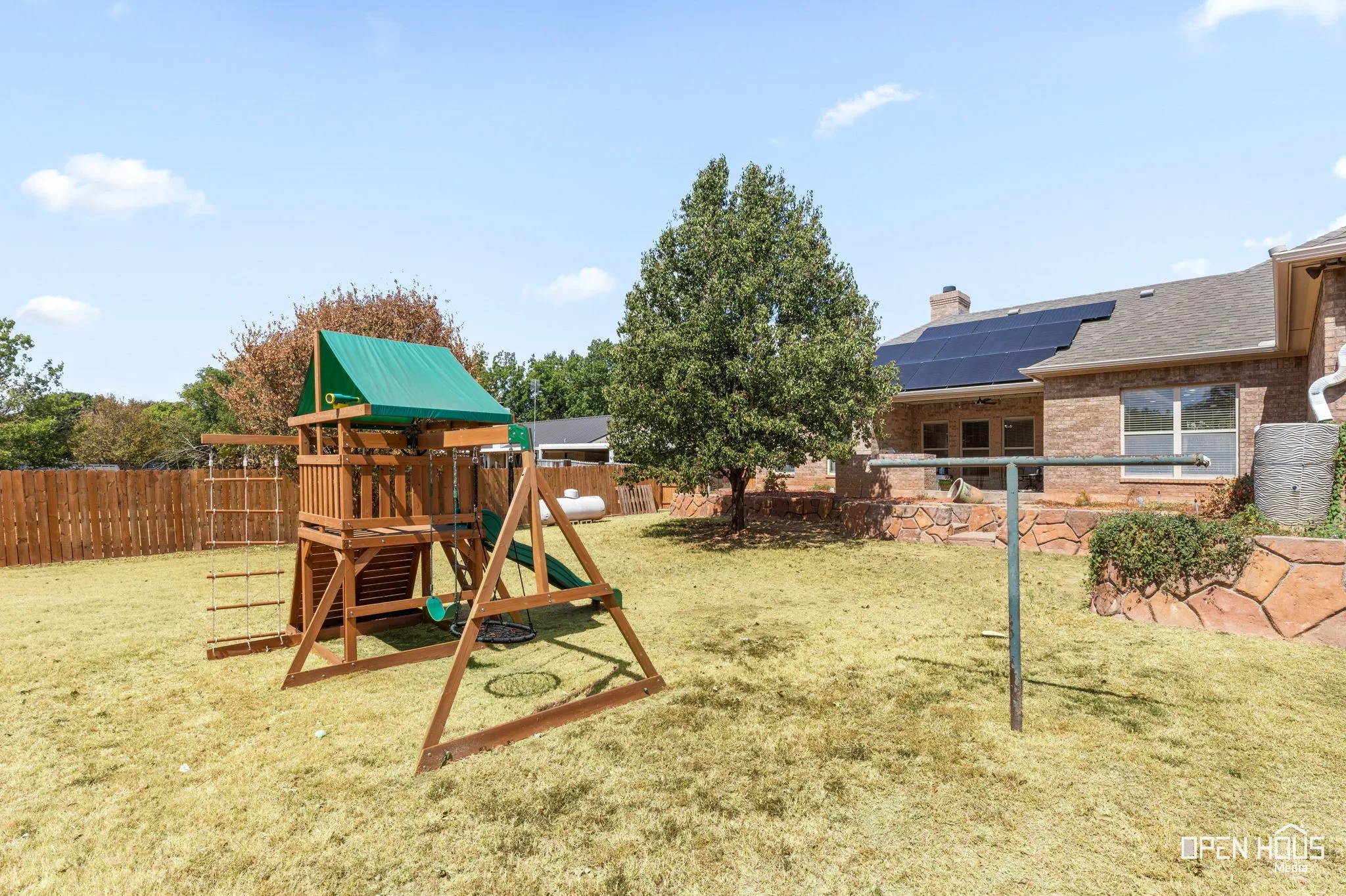 Expansive backyard featuring a wood privacy fence, a mature tree, a stone retaining wall, and solar panels on the roof