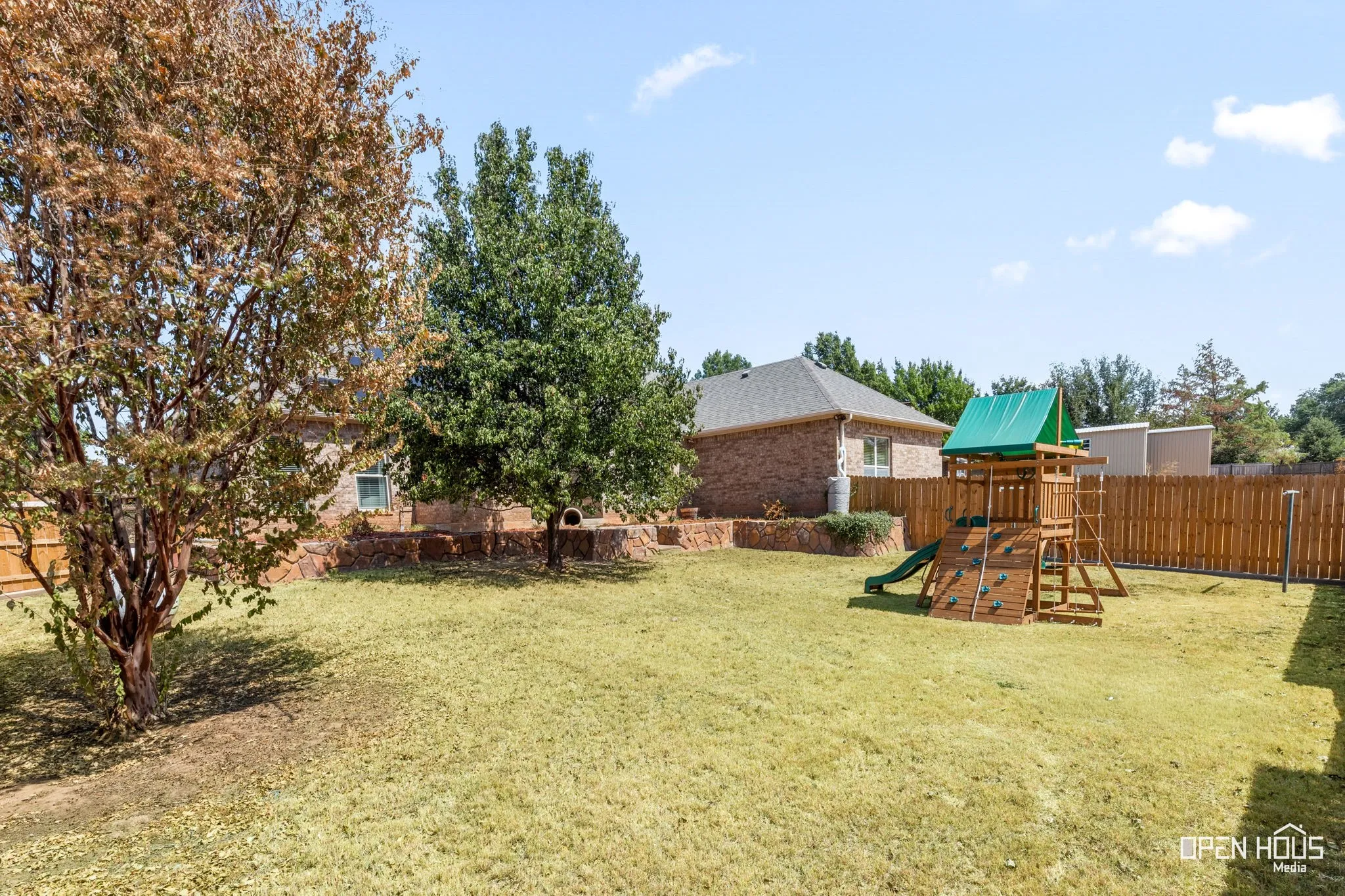Expansive grassy yard with a wooden privacy fence, mature trees, and a raised planter bed