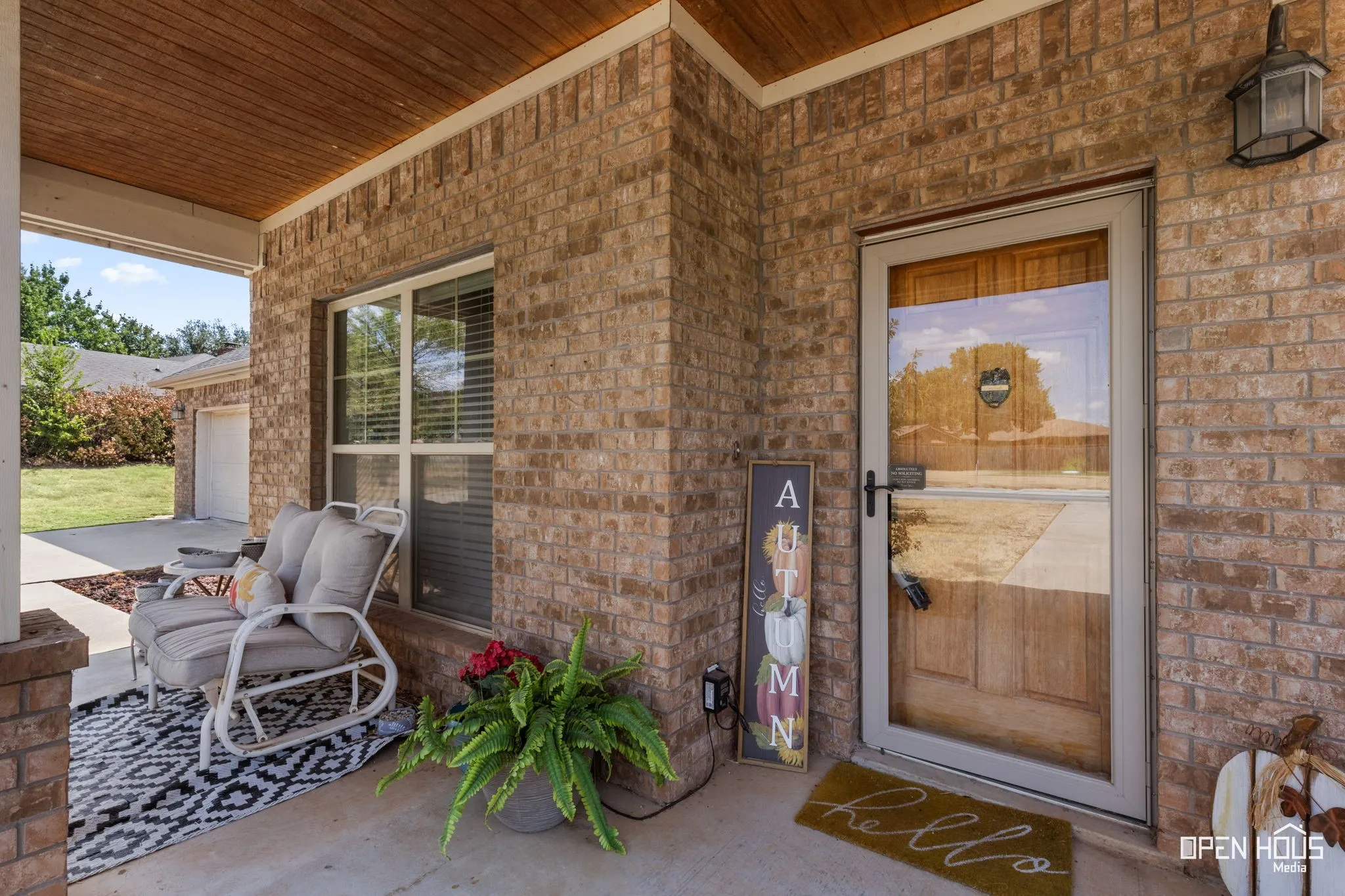 Brick exterior with a covered porch featuring a wood-panel ceiling, concrete flooring, and a storm door