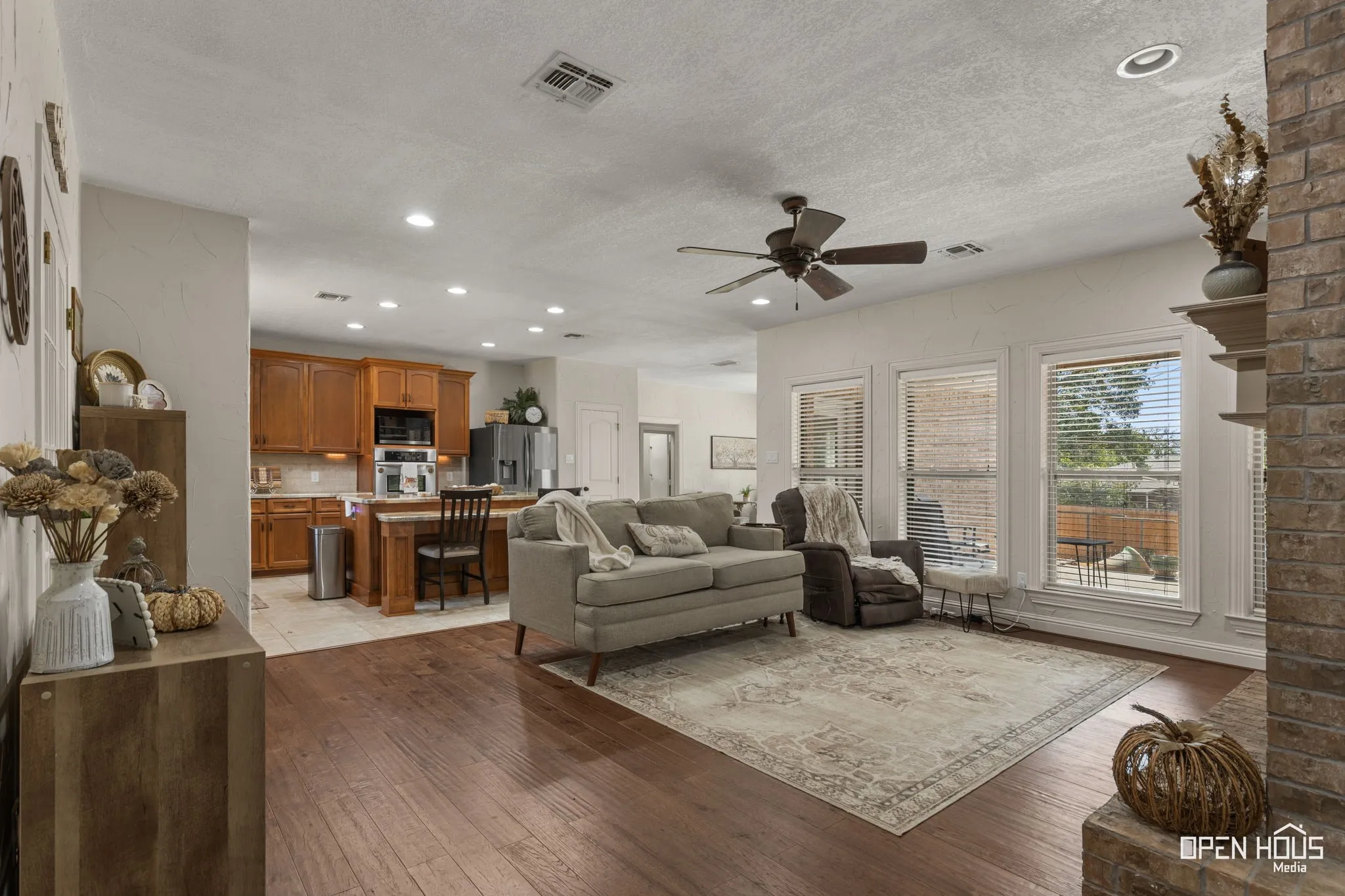 Hardwood flooring, recessed lighting, ceiling fan, brick fireplace, and multiple windows with blinds