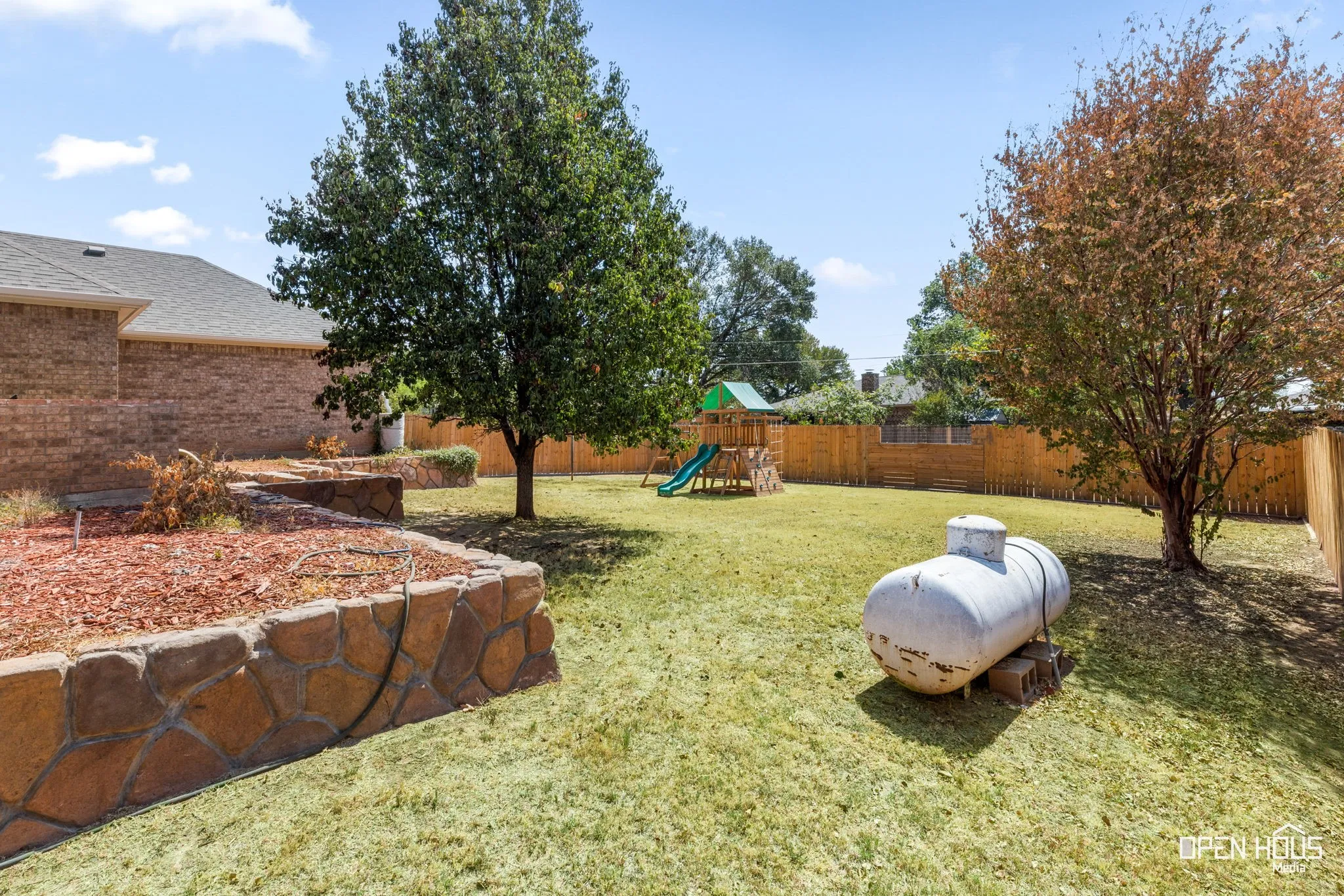 Expansive backyard with a manicured lawn, stone-faced retaining walls, a wood privacy fence, and mature trees