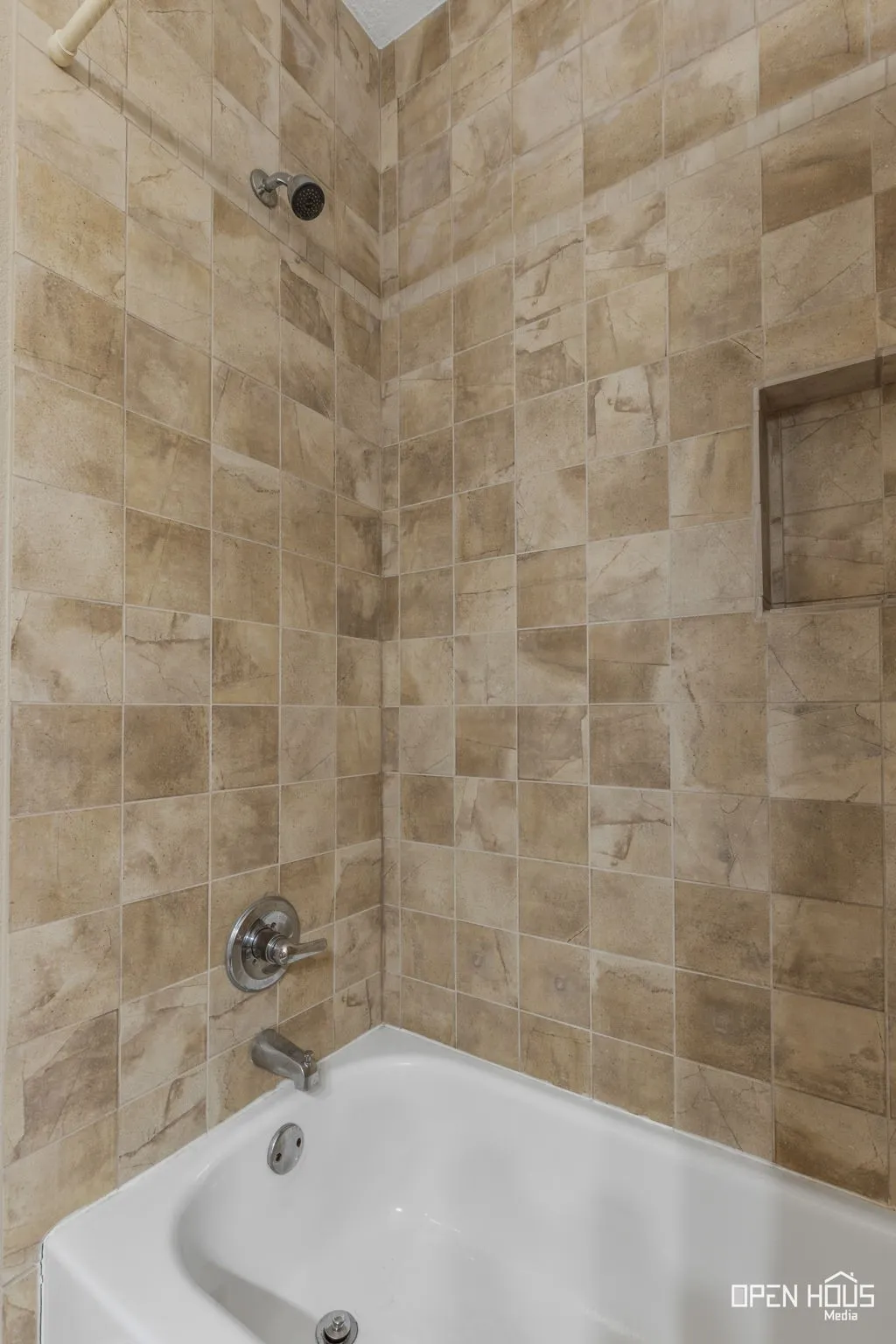 Bathtub with light-toned tiled surround, integrated shower niche, and chrome fixtures