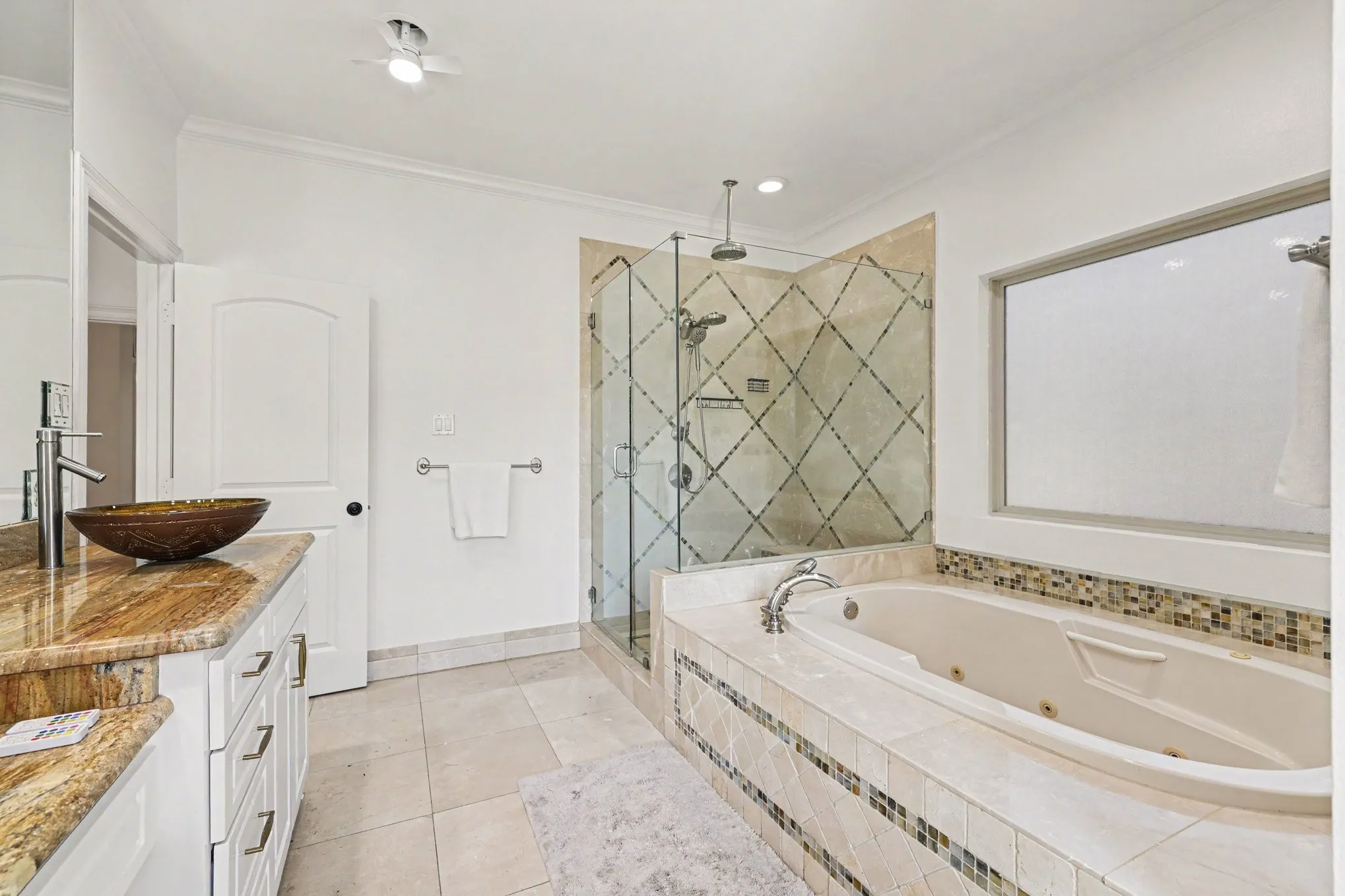 Spacious bathroom featuring a glass-enclosed shower, a large soaking tub, a vanity with a vessel sink, and an expansive window