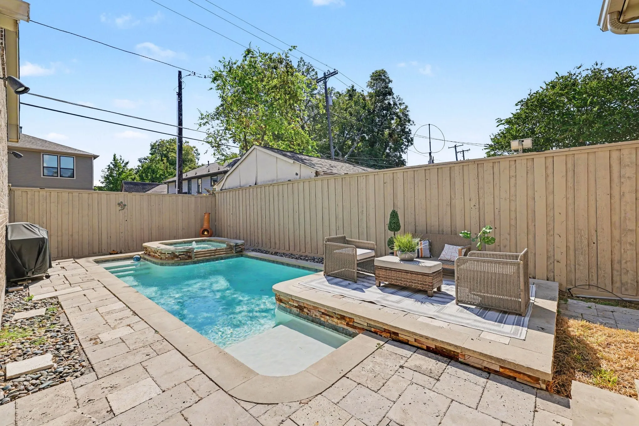 Outdoor pool with integrated spa and stone surround, accompanied by an elevated patio area and wood privacy fencing