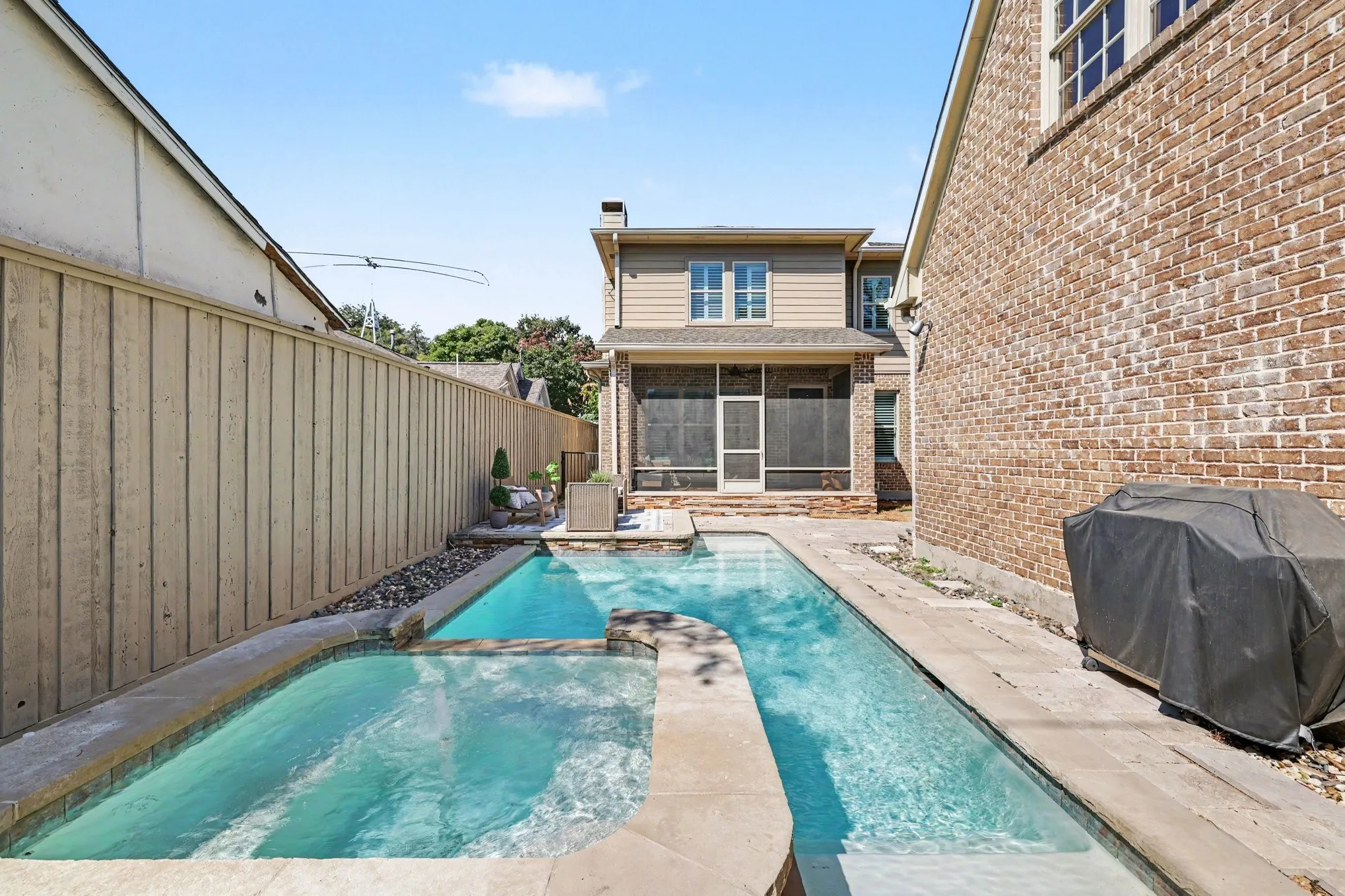 Backyard featuring a rectangular swimming pool, integrated spa, stone coping, privacy fencing, and a screened porch