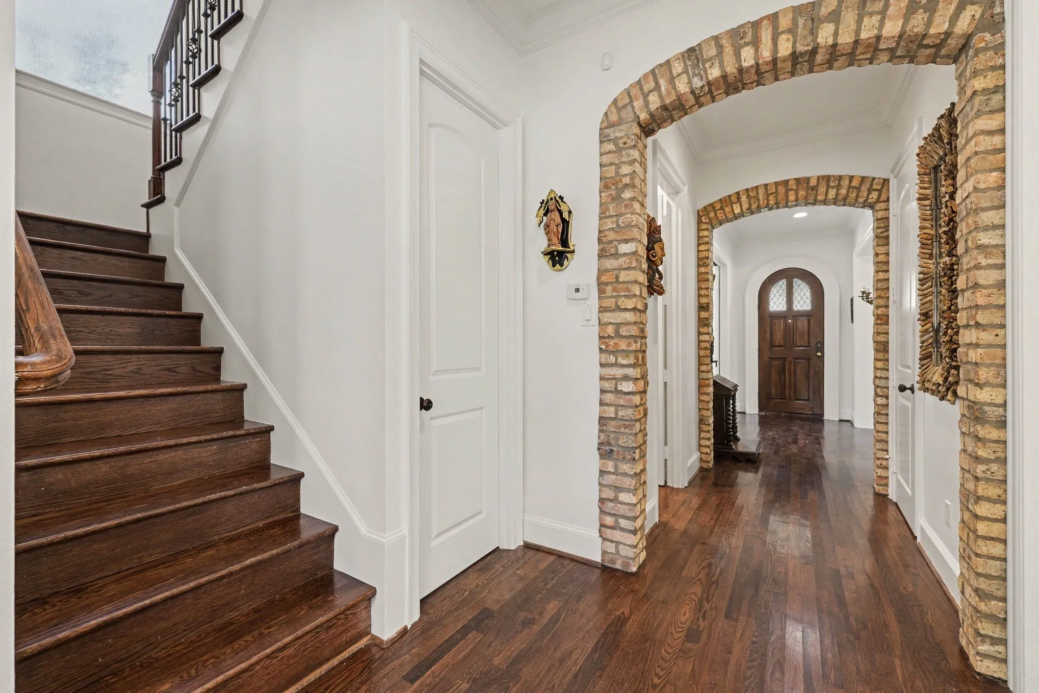Wood-finish flooring throughout, brick archways, white paneled doors, and a staircase with dark wood treads and an ornate railing