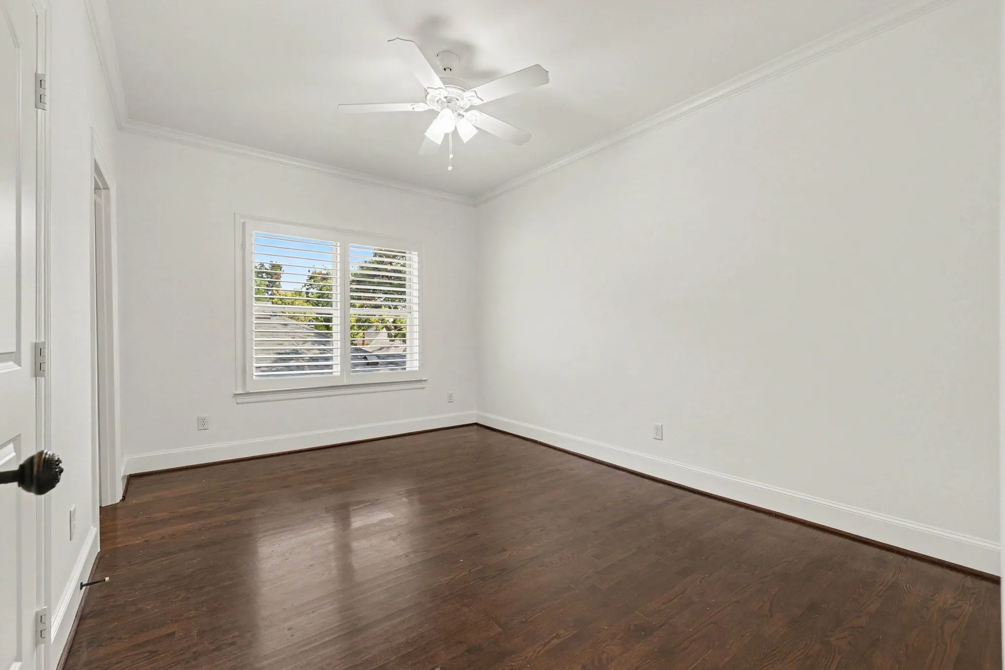 Hardwood flooring, window with plantation shutters, ceiling fan, crown molding, white painted walls