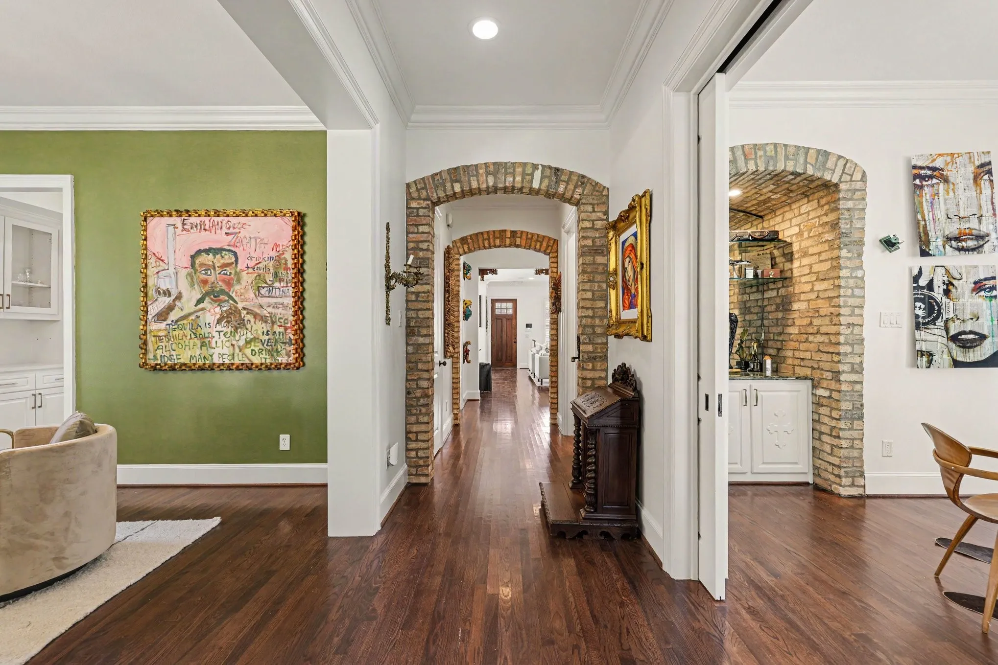 Rich wood-finish flooring, brick archways, white crown molding, and recessed lighting