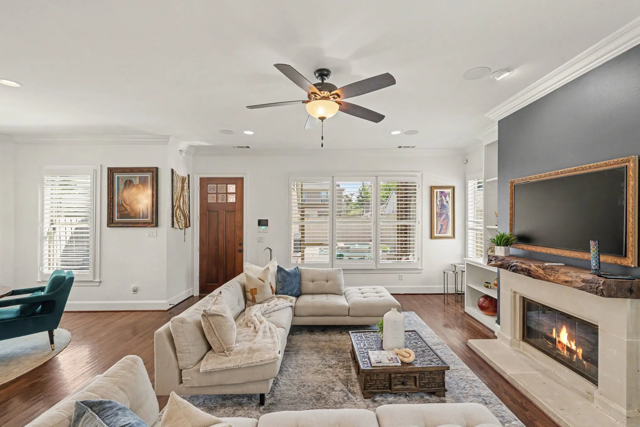 Hardwood flooring, crown molding, ceiling fan, natural light from multiple windows, and a built-in fireplace with a stone surround